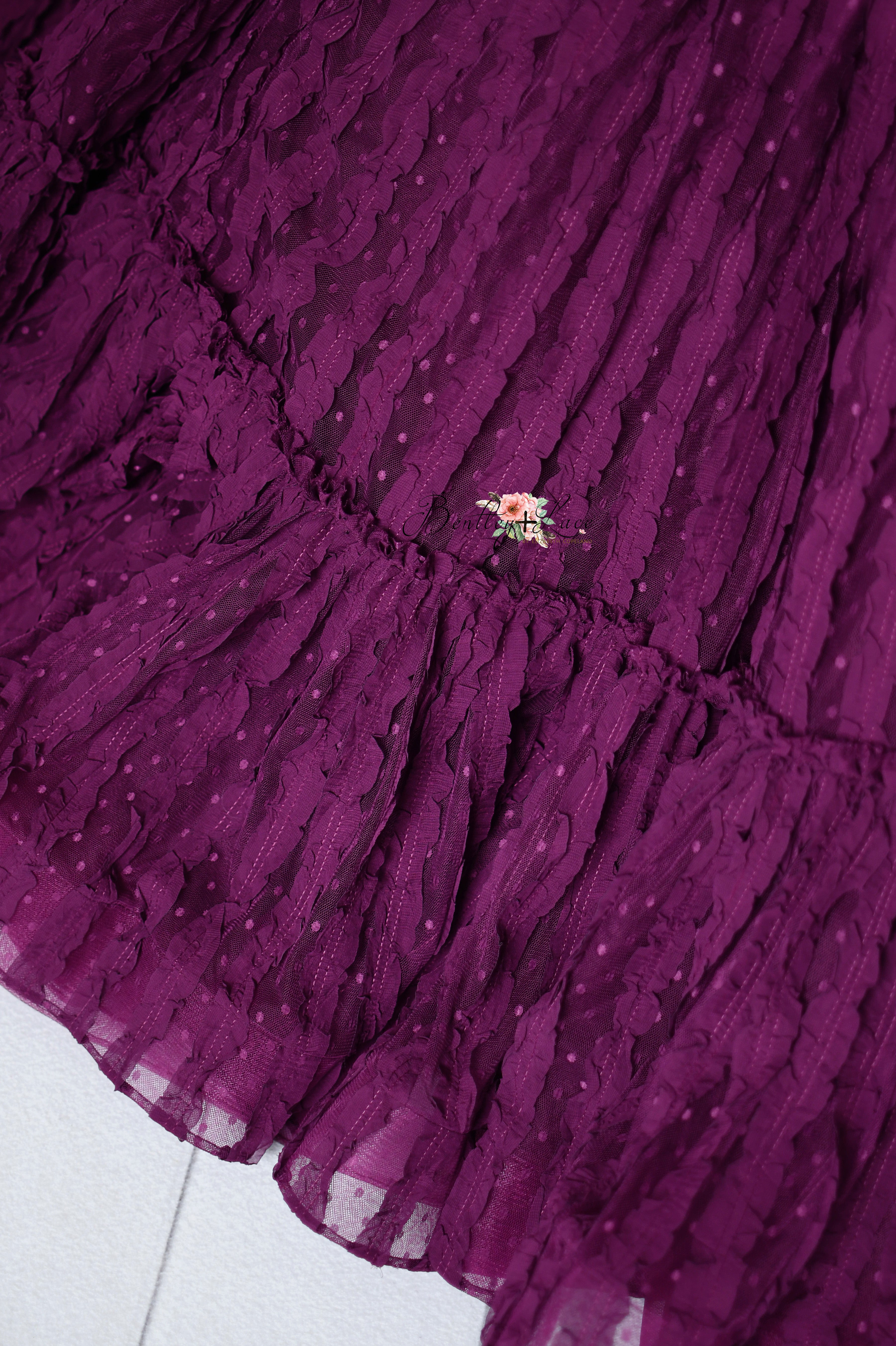 Child’s couture dress in a deep berry hue, featuring a layered, ruffled design with dotted lace accents.
