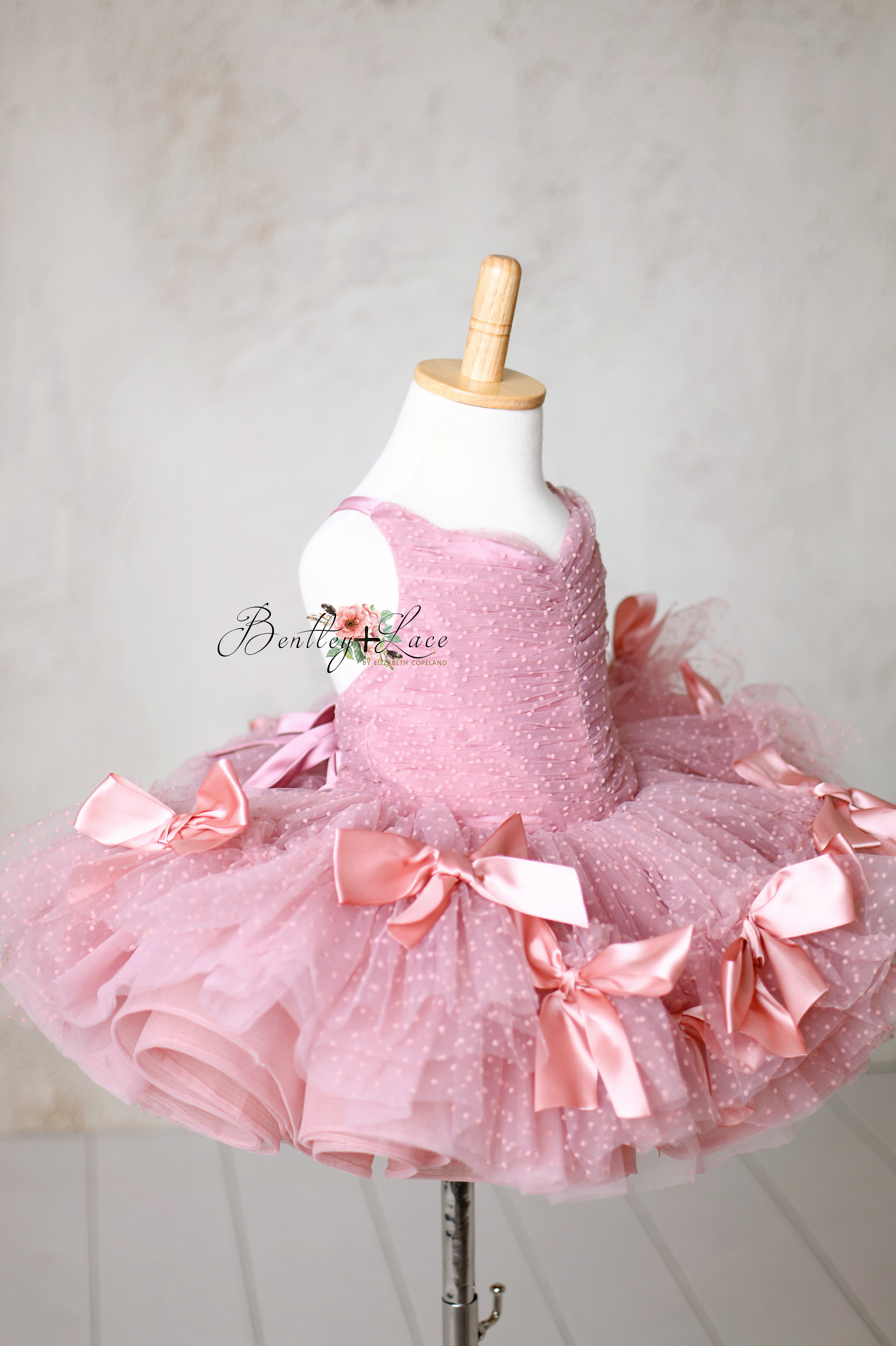 Whimsical pink dress with ruched detailing and fluffy tulle layers adorned with satin bows.
