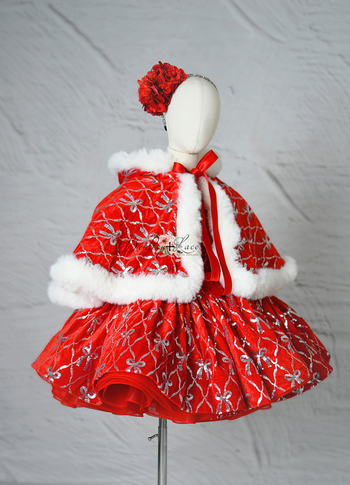 Red velvet holiday dress with silver embroidered bows and puff sleeves displayed on mannequin.