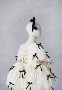 Luxury children's gown in cream with detachable sleeves and black ribbon accents, ideal for styled photo sessions.

