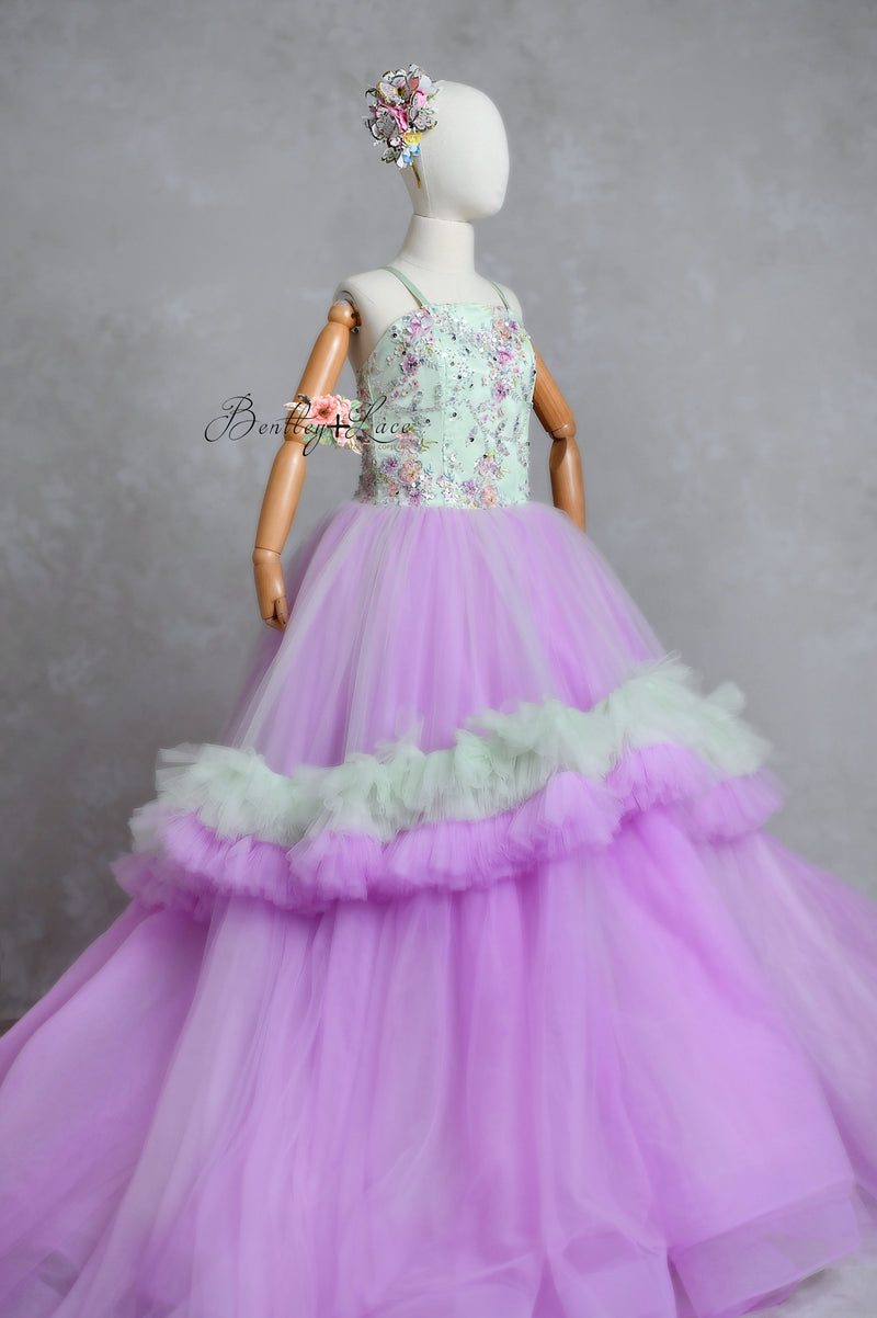 A floor-length gown with a floral pattern on the bodice and a solid purple tulle skirt with a petticoat underneath. The dress features shoulder ties and an elastic waist.