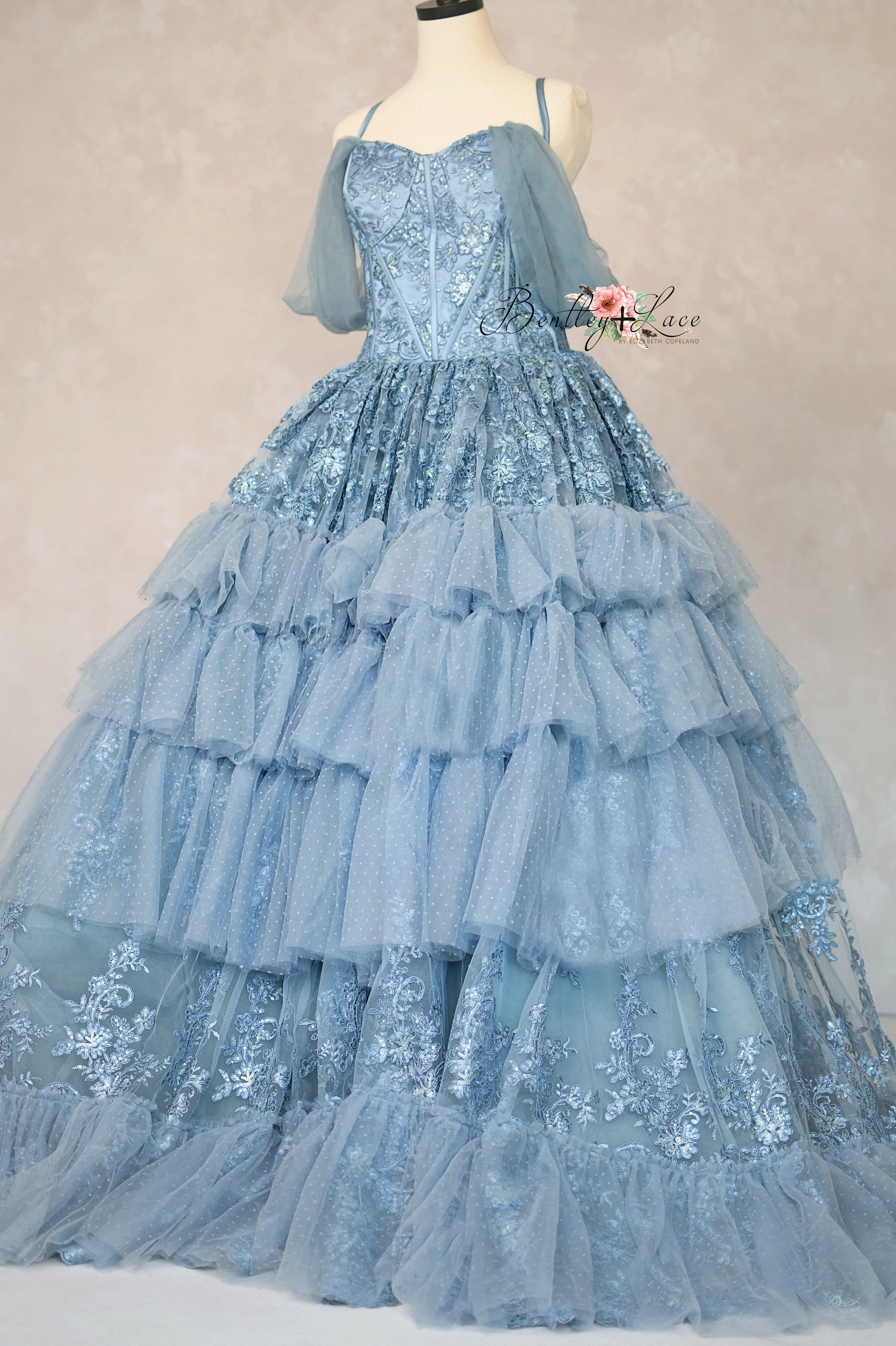 Blue lace gown on a mannequin against a plain background