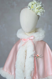 Mannequin wearing a pink cape with white fur trim and floral headband against a gray background.