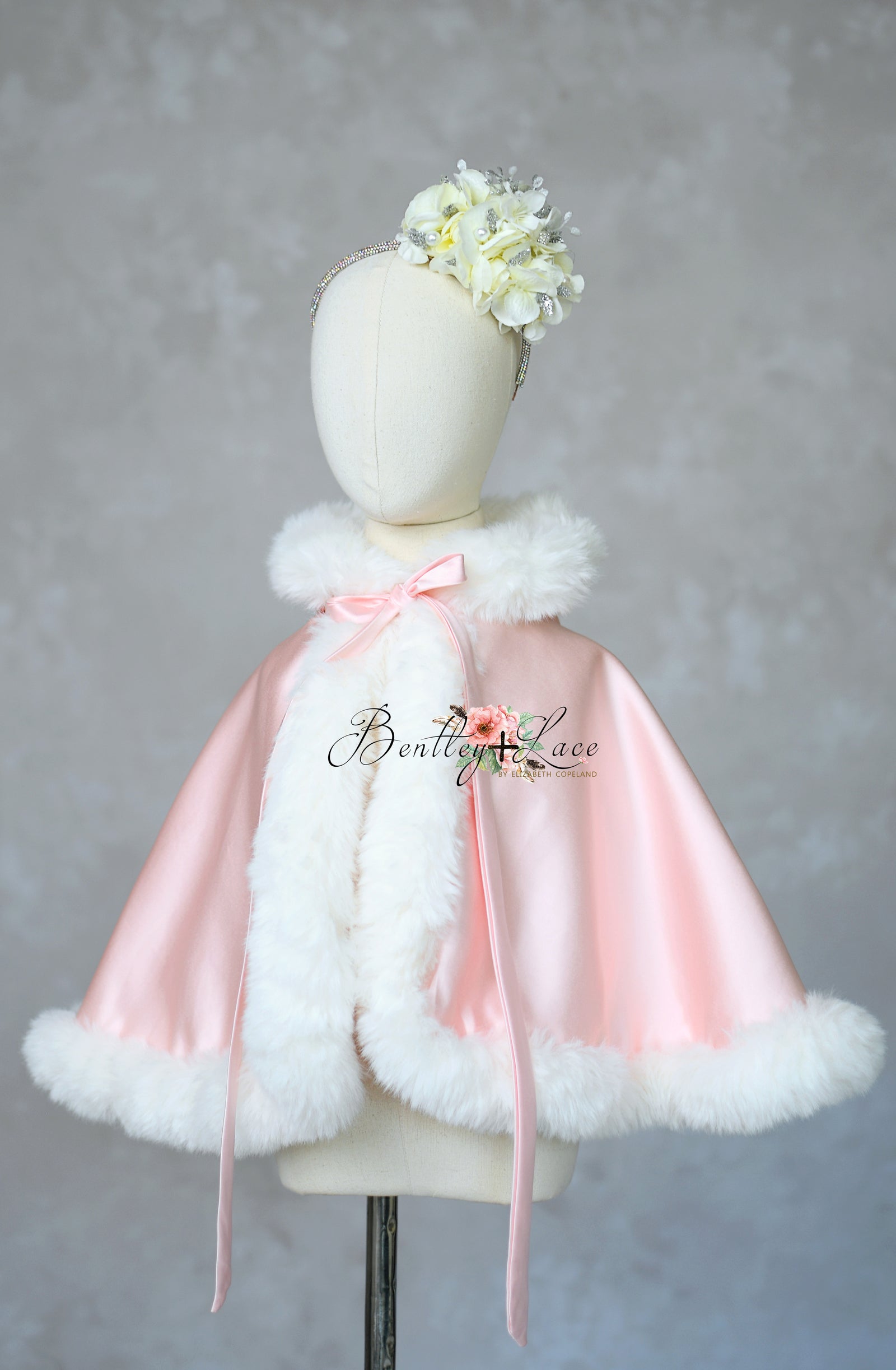 Pink cape with white fur trim on a mannequin against a gray background