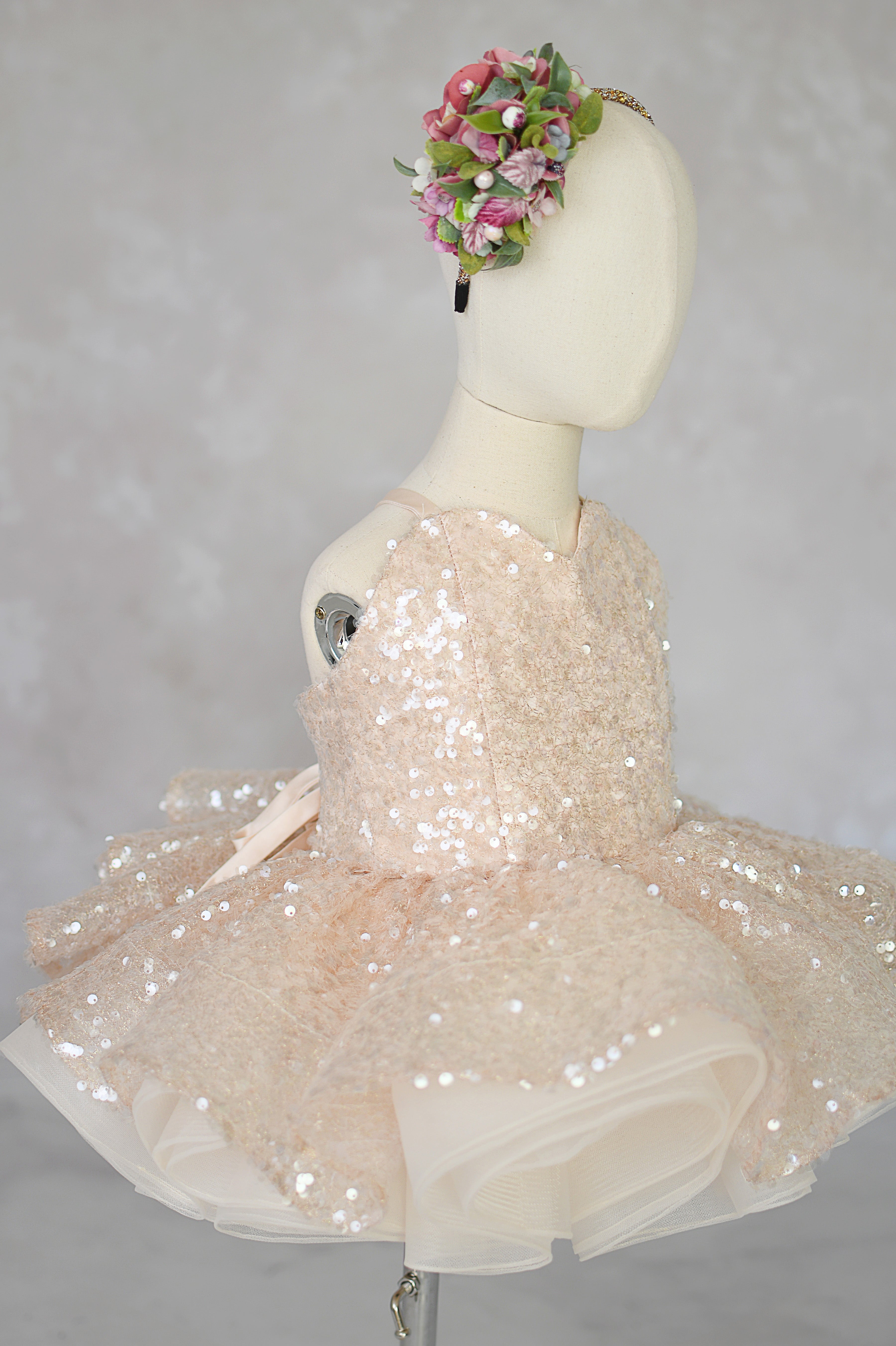 Beige sequin dress on a mannequin with a floral headband against a gray background