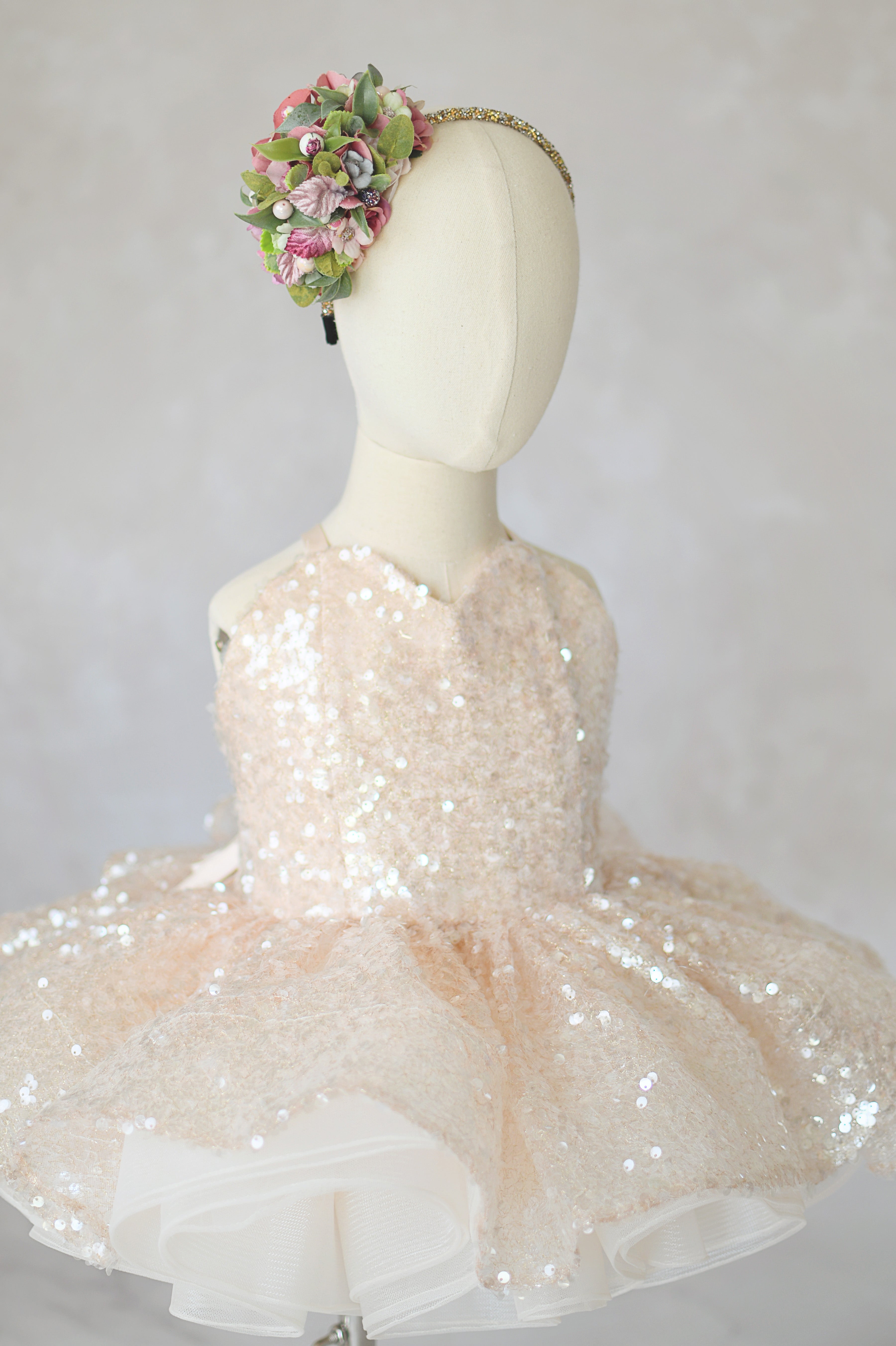 Mannequin wearing a beige sequined dress with a floral headband on a light gray background