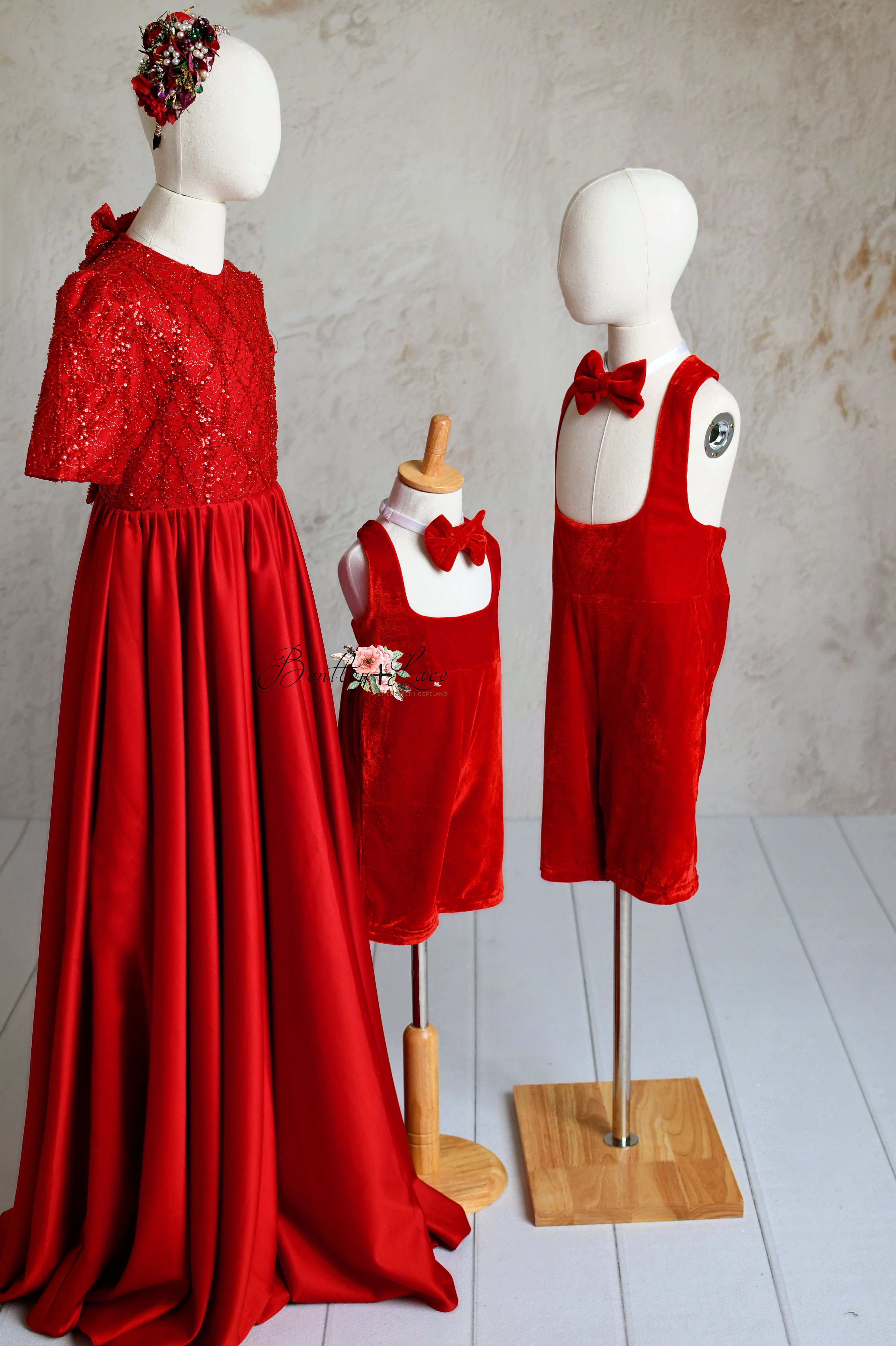 Matching red velvet suspender outfits for children displayed on mannequins, featuring bow ties.