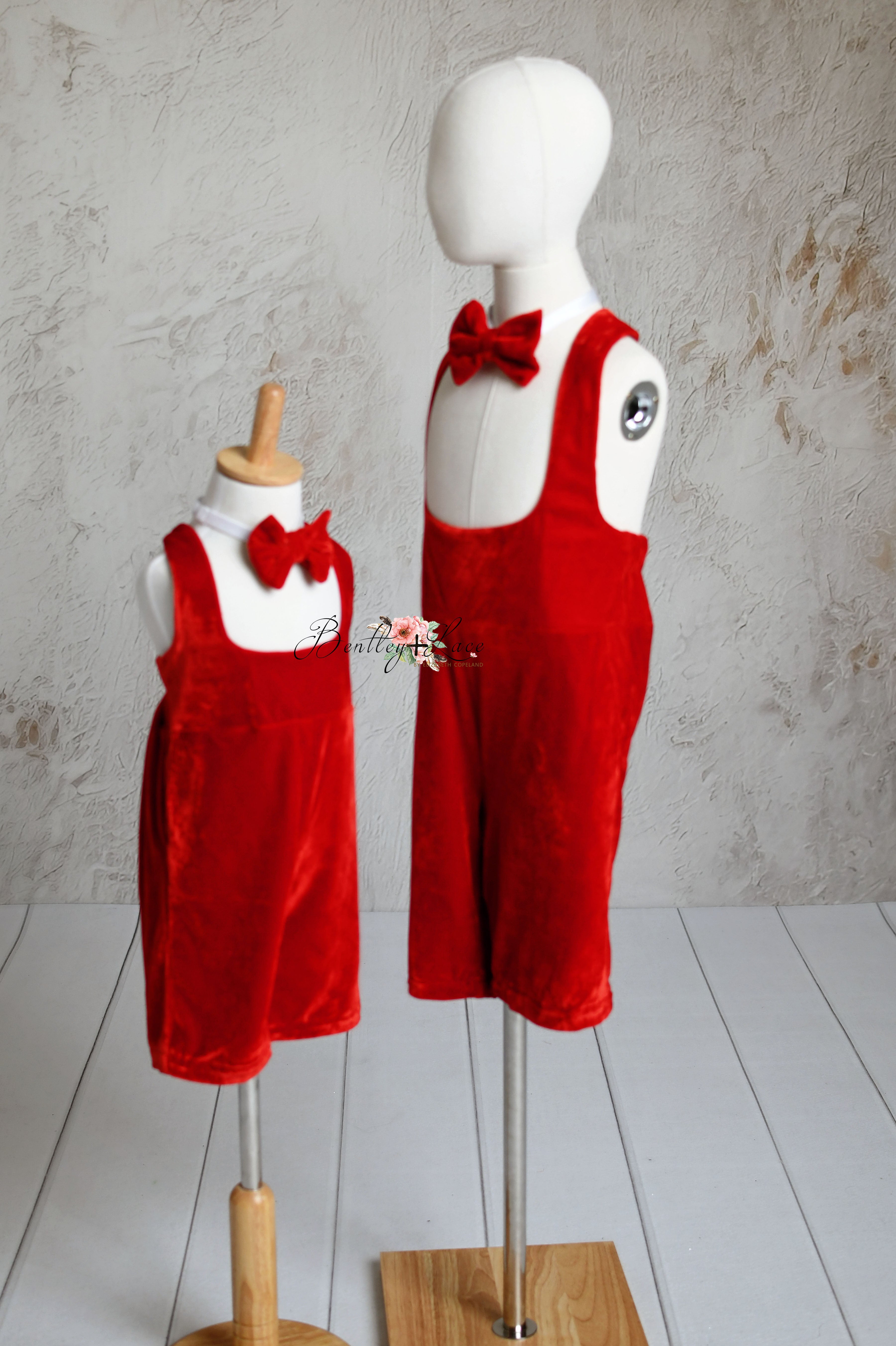 Children's red velvet suspender outfits with bow ties, shown on standing mannequins.