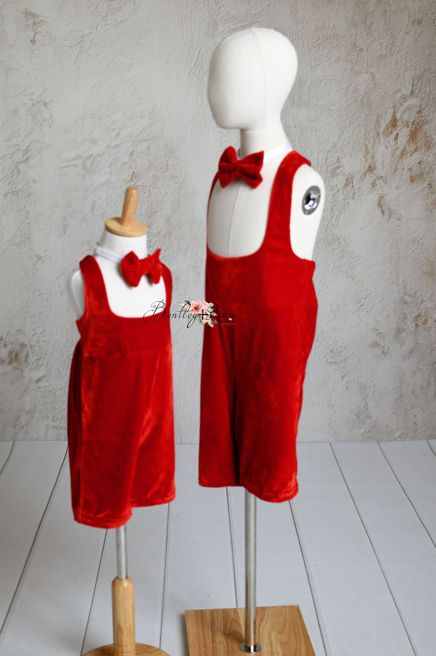 Children's red velvet suspender outfits with bow ties, shown on standing mannequins.