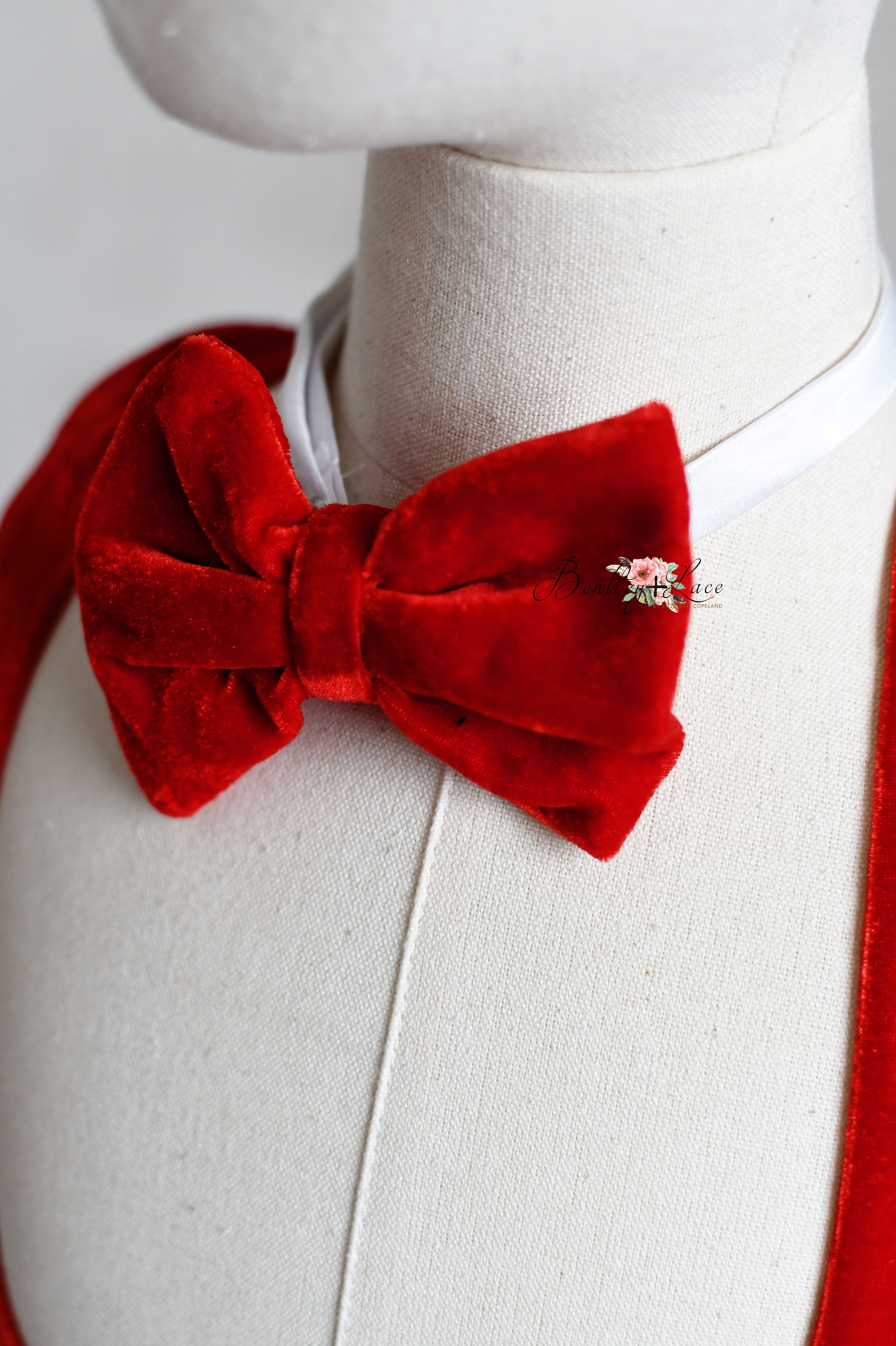 Matching set of red velvet toddler outfits, featuring suspenders and bow ties, displayed on mannequins.