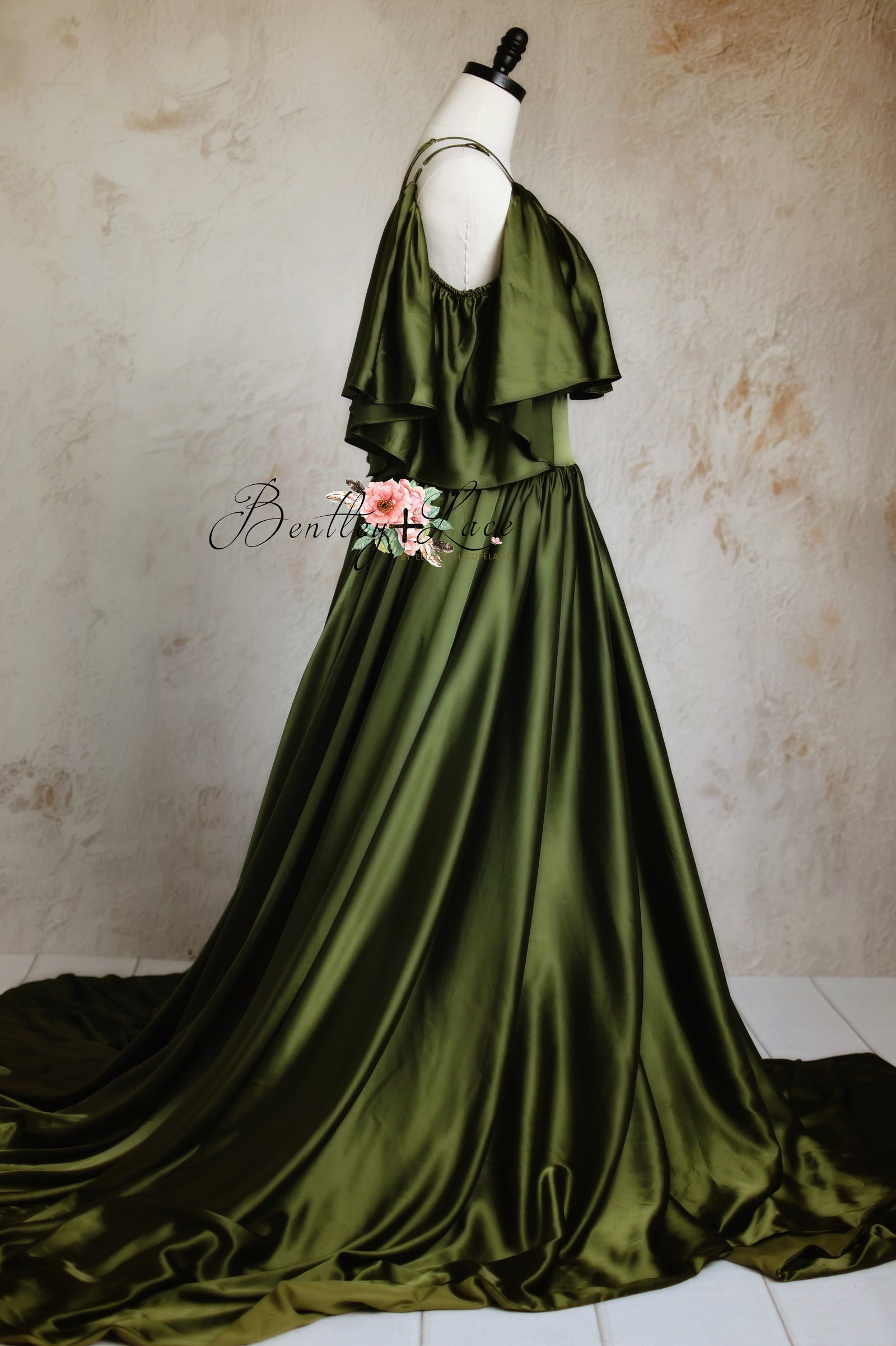 Dramatic green dress with a floor-sweeping train, displayed against a dreamy pink and gray backdrop.
