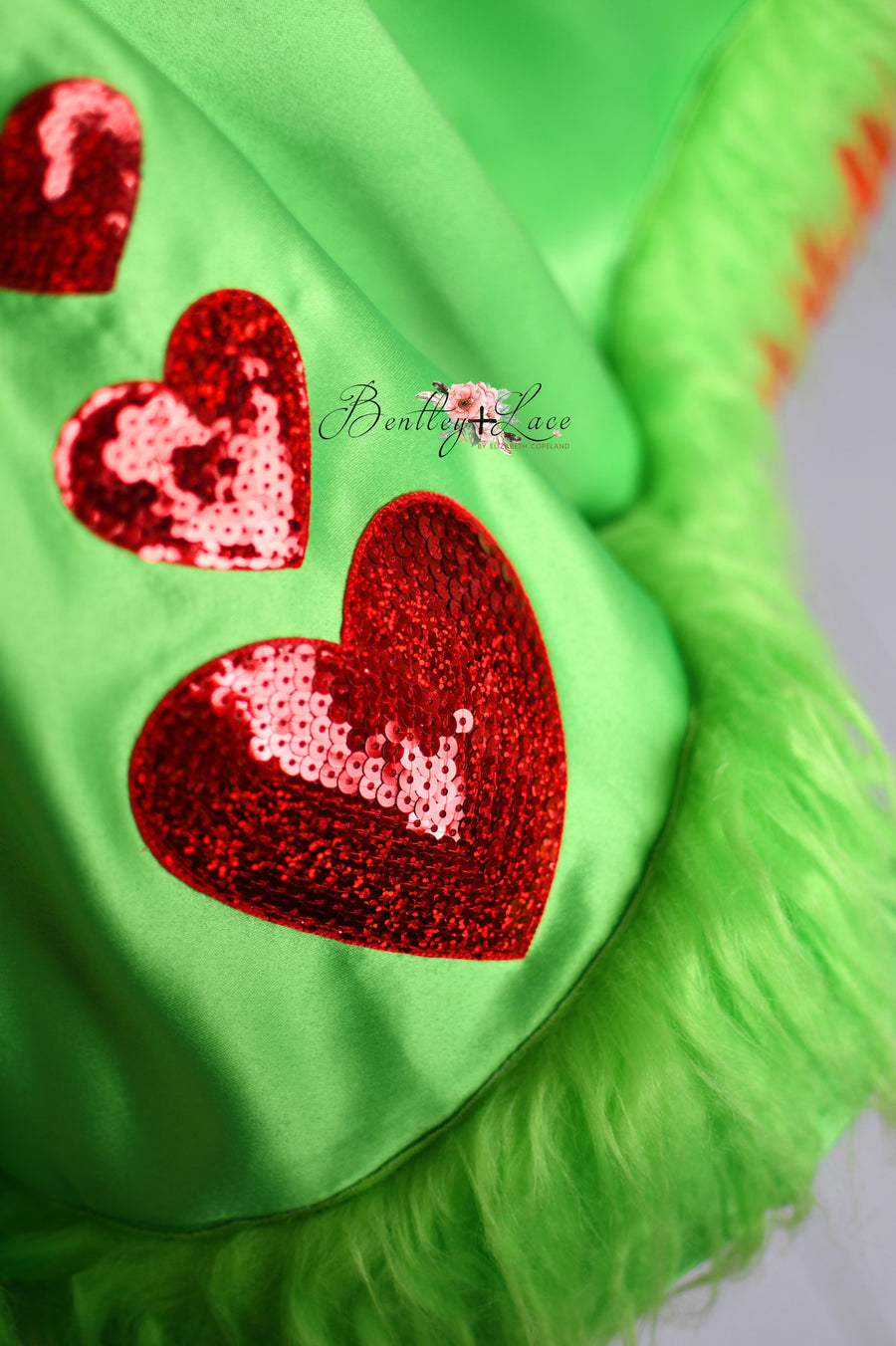 Children's holiday dress with red satin fabric, detachable themed apron, and fluffy green trim for a festive look.

