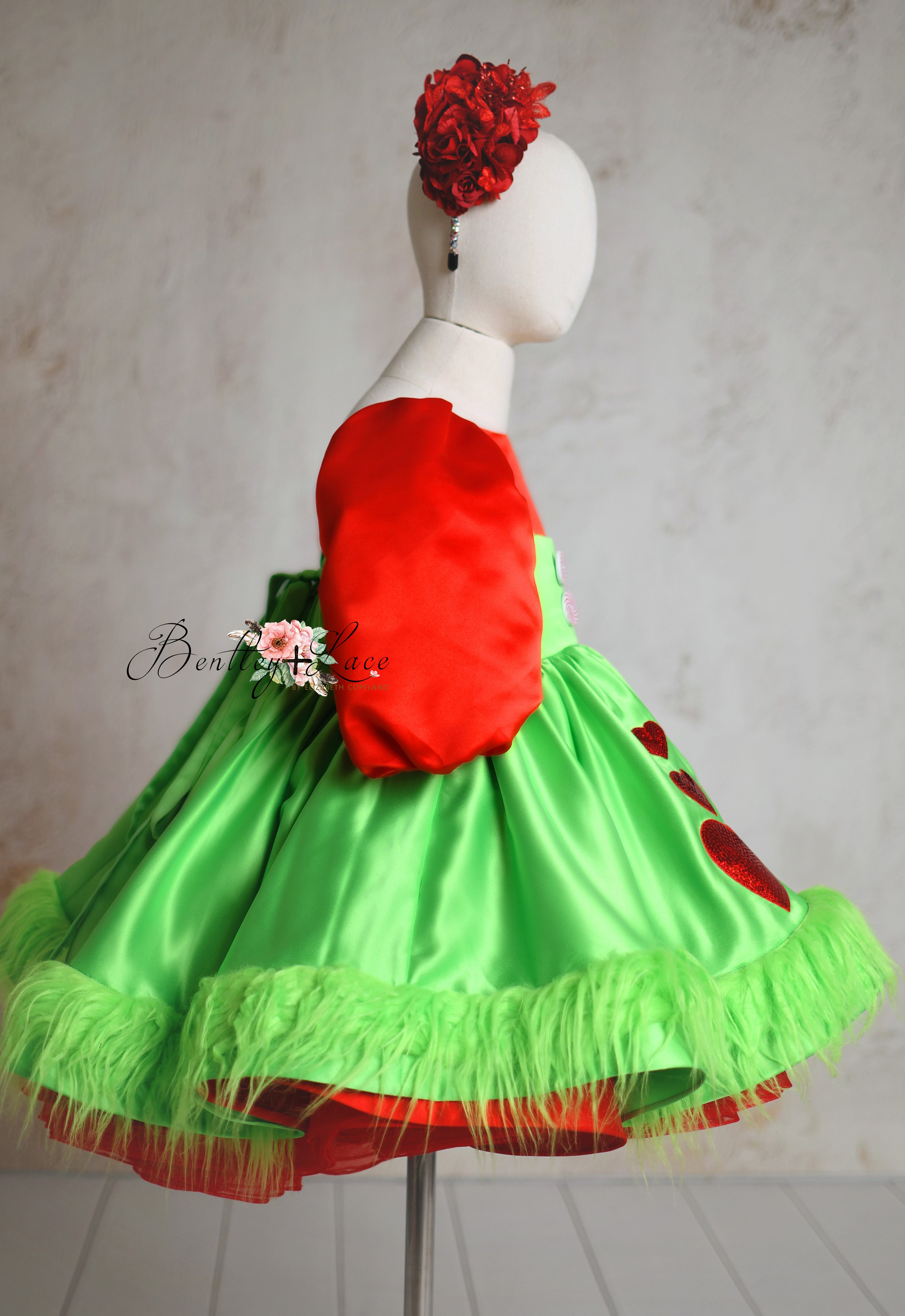 Festive red satin dress with puffed sleeves and a playful green apron adorned with whimsical holiday details.
