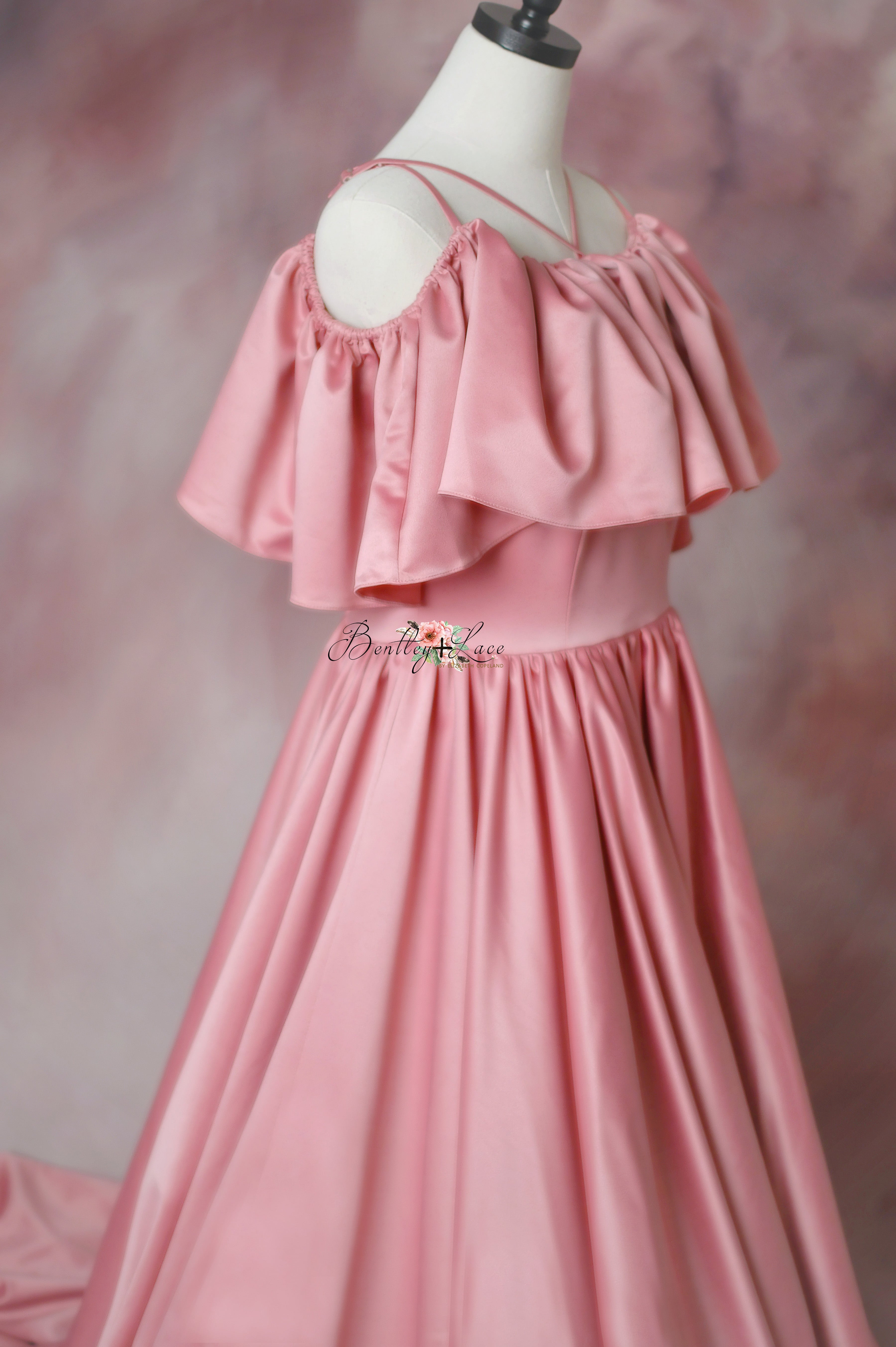 Side profile of an elegant pink satin gown with a flowing skirt and decorative neckline.