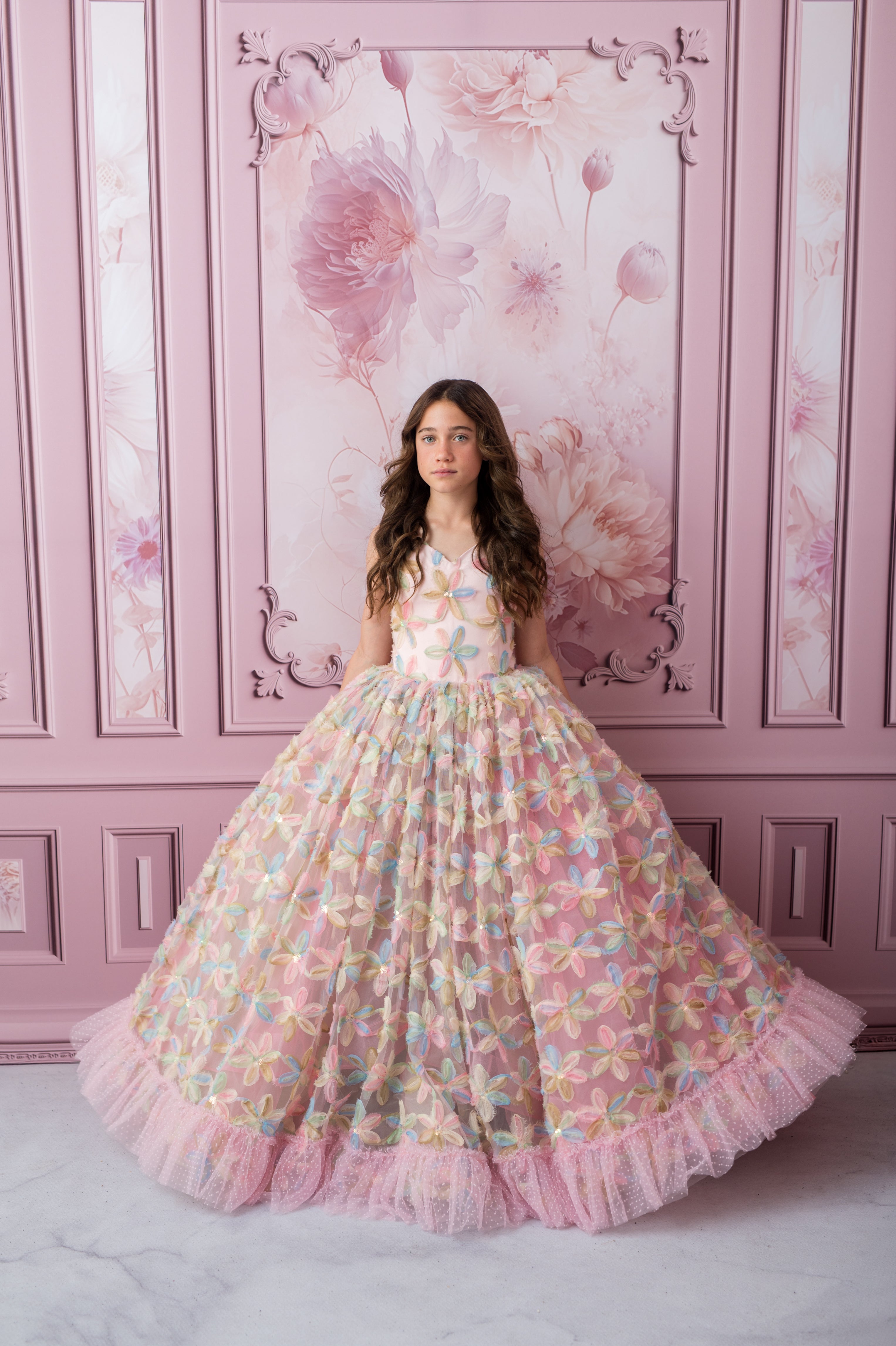 Woman in a floral dress standing against a pink floral wall.