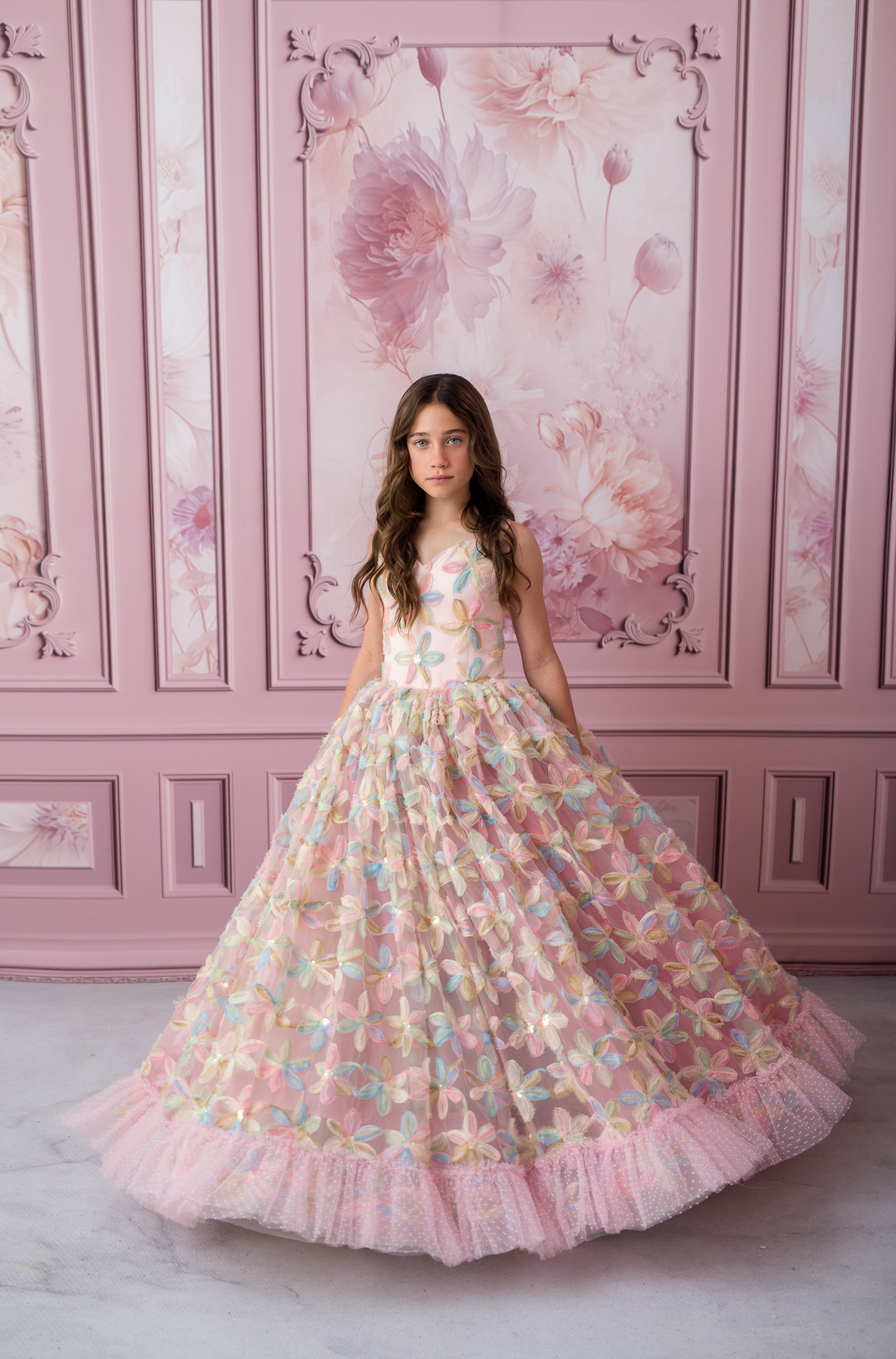 Woman in a floral dress standing against a pink floral wall.