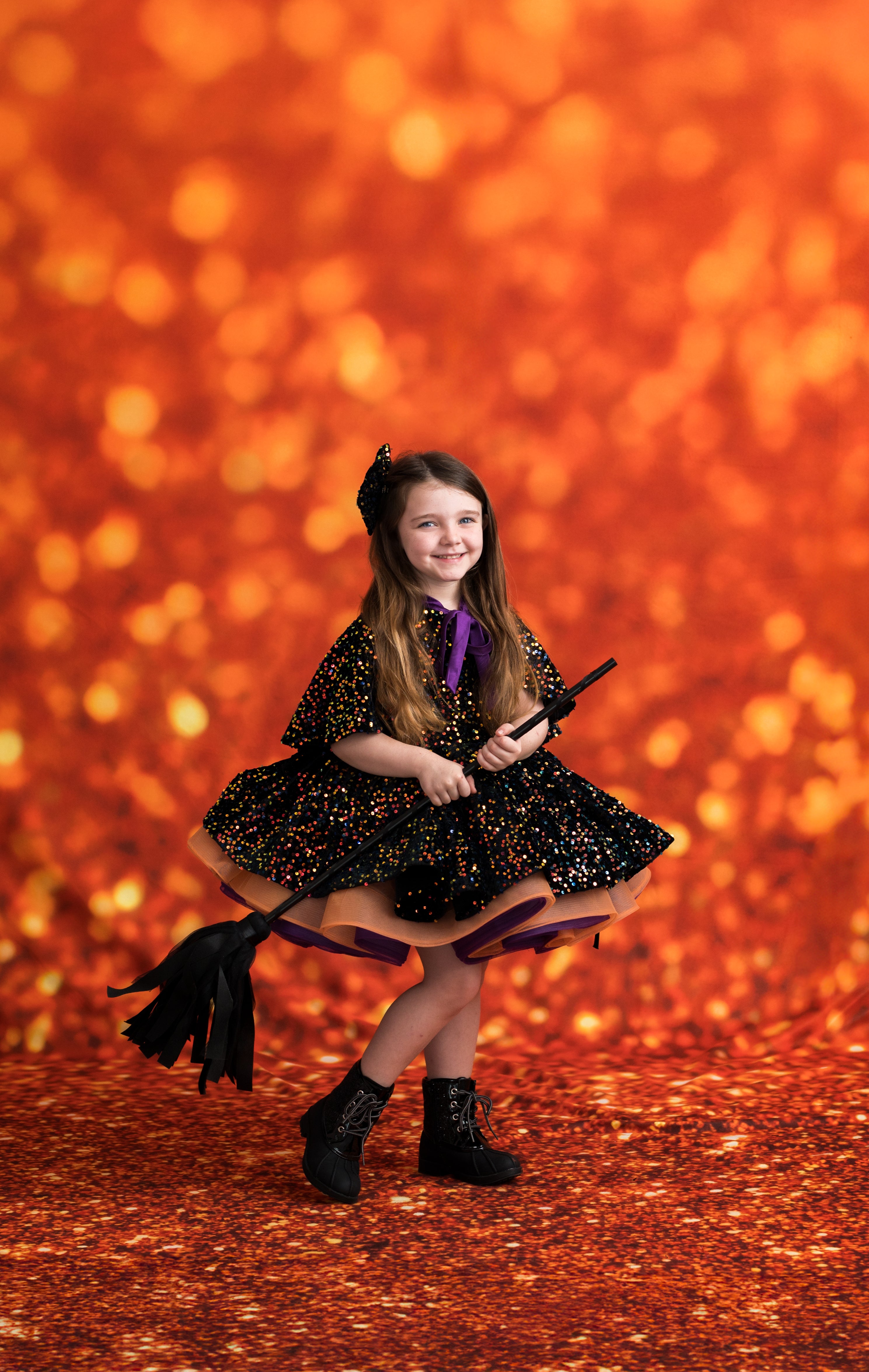 Young girl in a Halloween costume with a broom against an orange glittery background