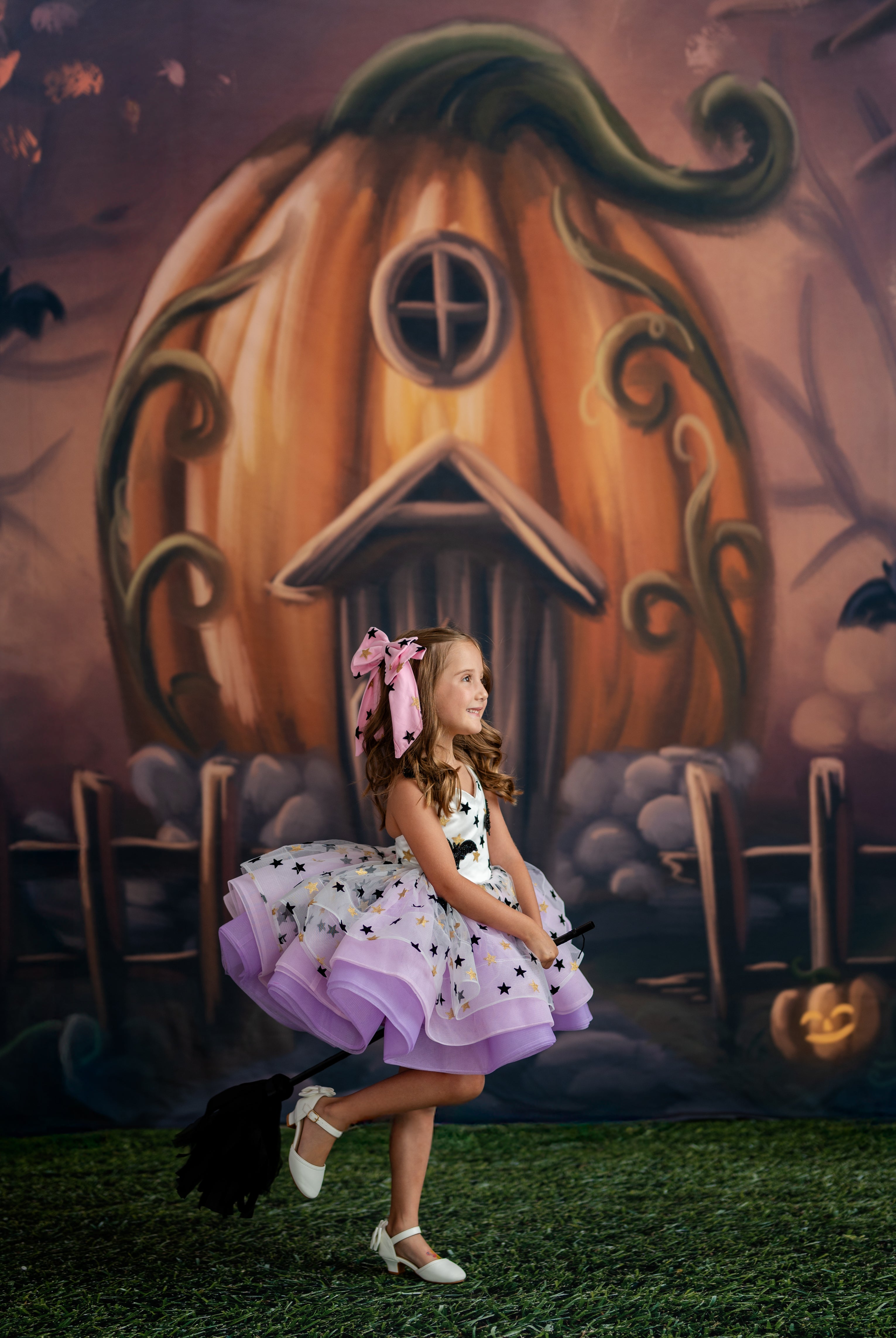 Young girl in a purple dress standing in front of a pumpkin house backdrop