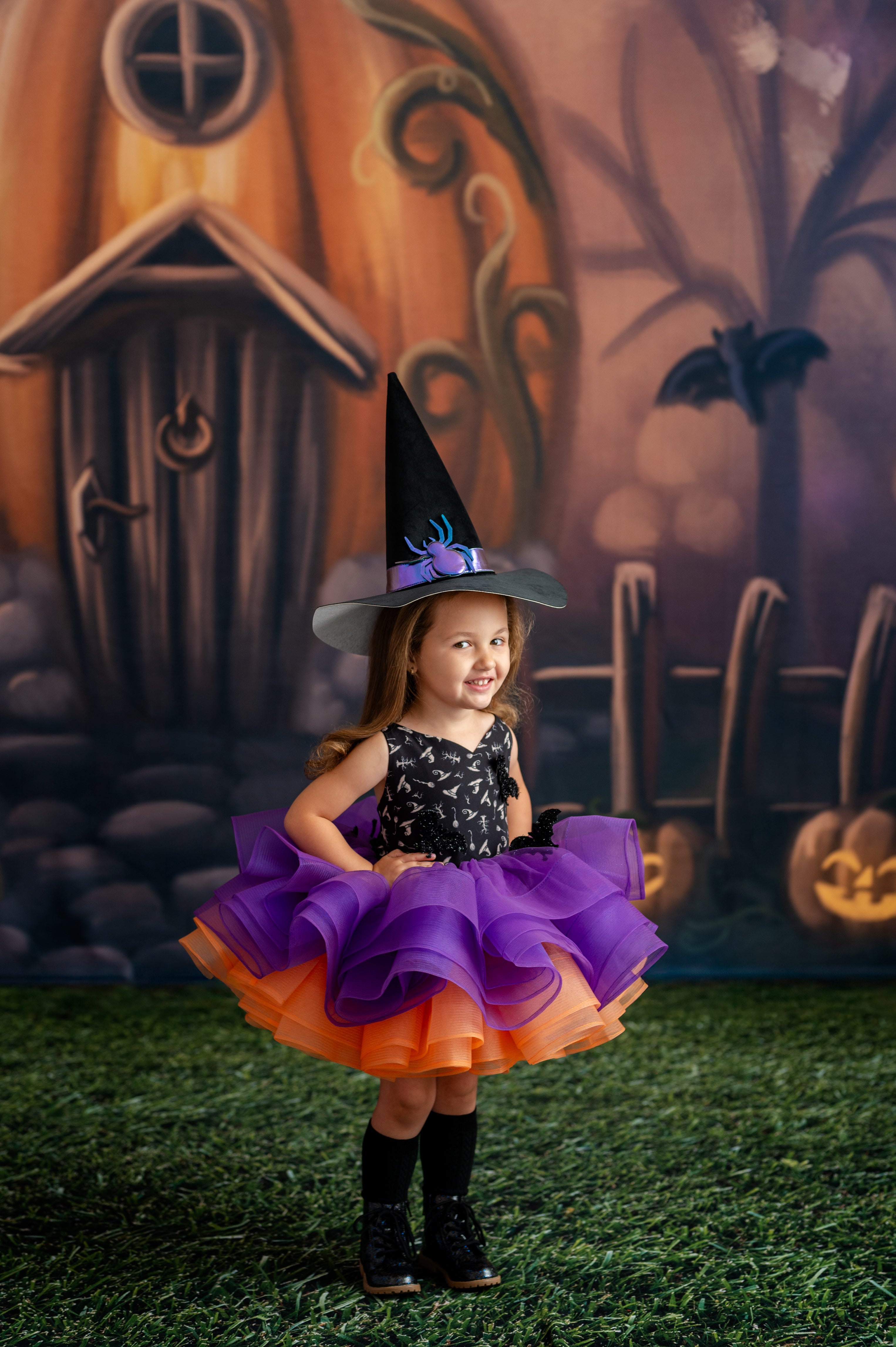 Child in a Halloween witch costume with a decorated pumpkin house in the background