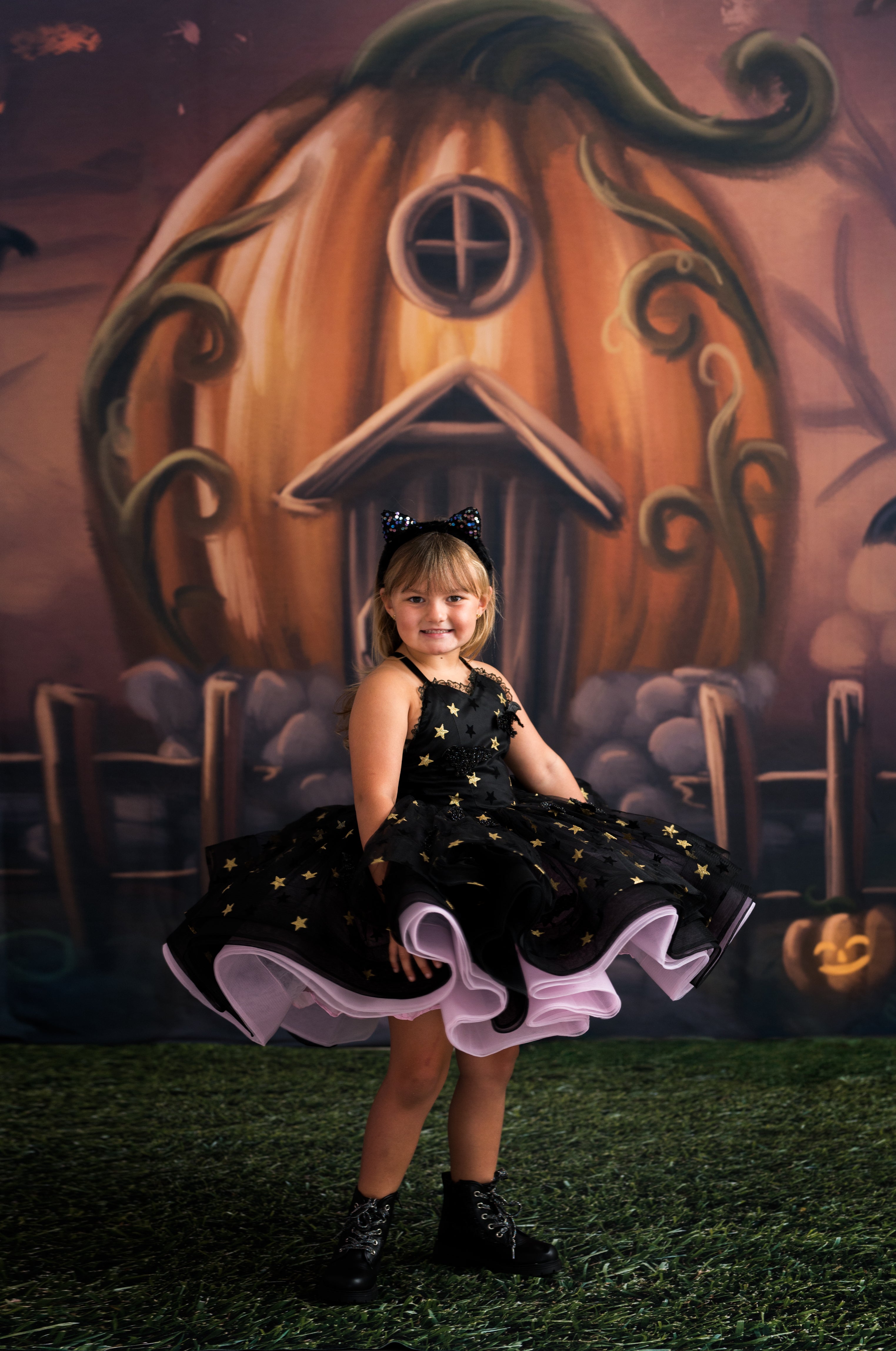 Child in a black dress with white accents sitting in front of a large decorative pumpkin.