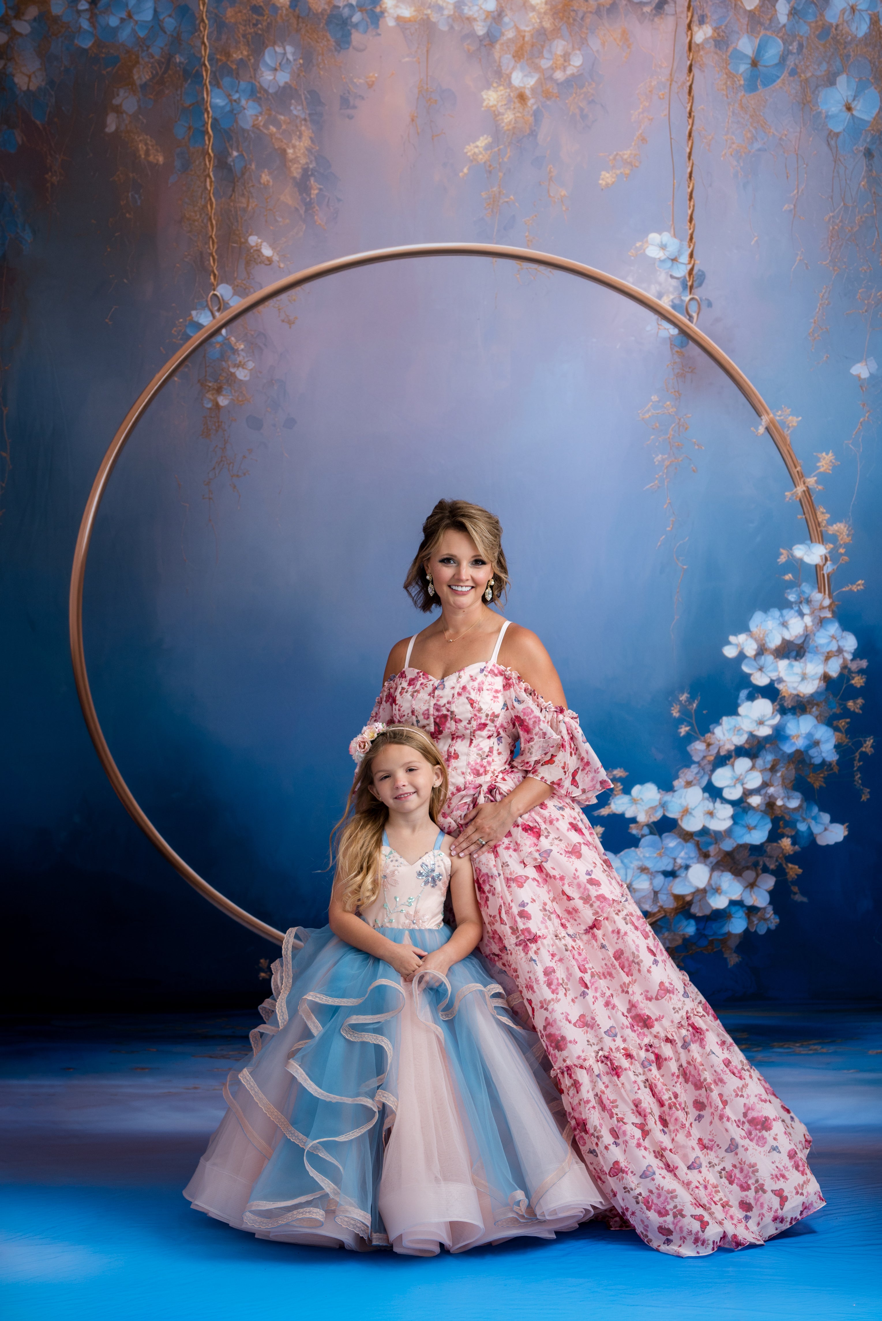Woman and young girl in formal dresses posing in front of a floral arch.