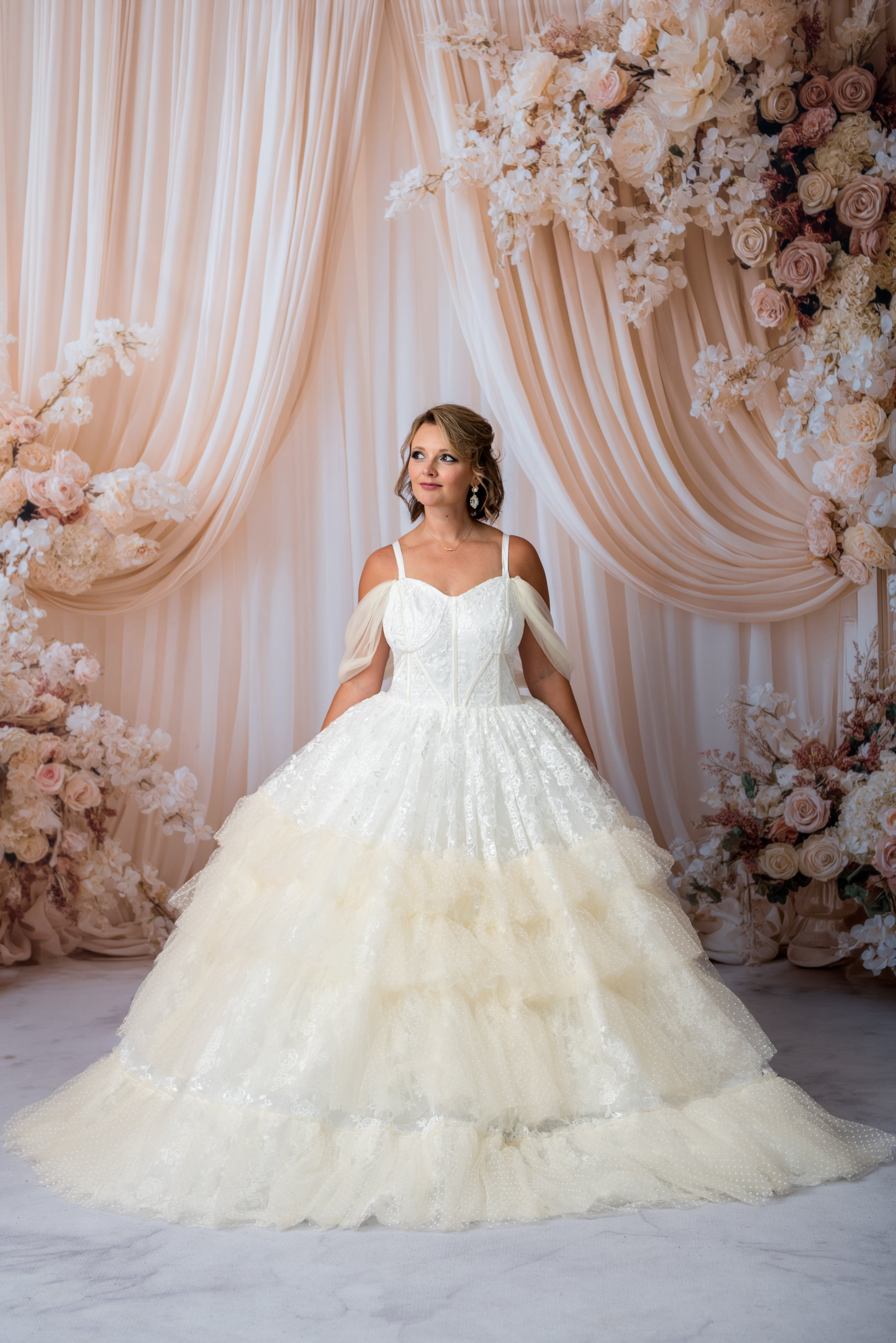 Woman in a white wedding dress standing in front of a floral and drapery backdrop