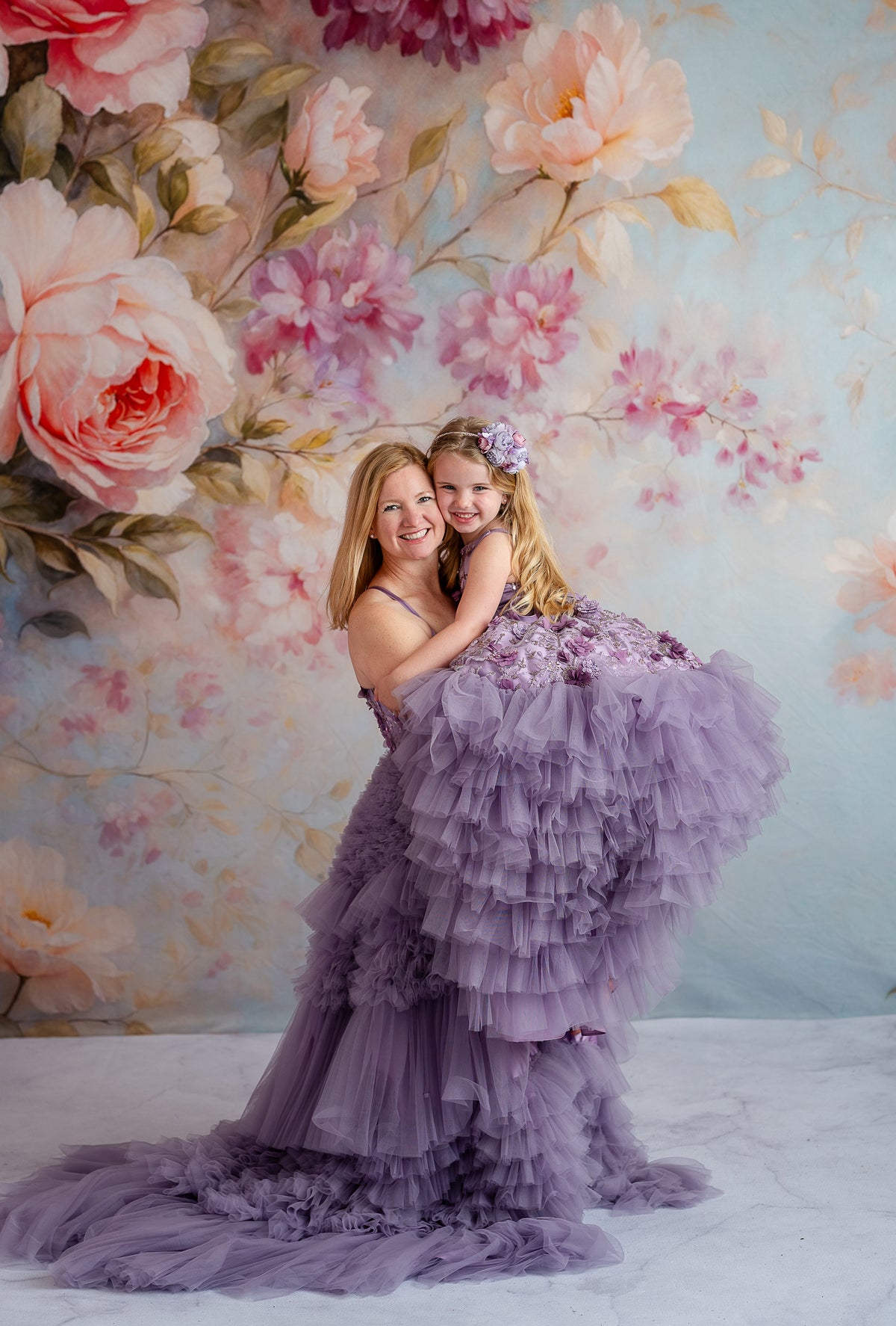 Close-up of mom and daughter embracing in Violet Grace gowns with floral appliqués.

