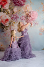 Whimsical fashion shot of a woman in a dramatic lavender dress and crown, standing in a white palace-style room.

