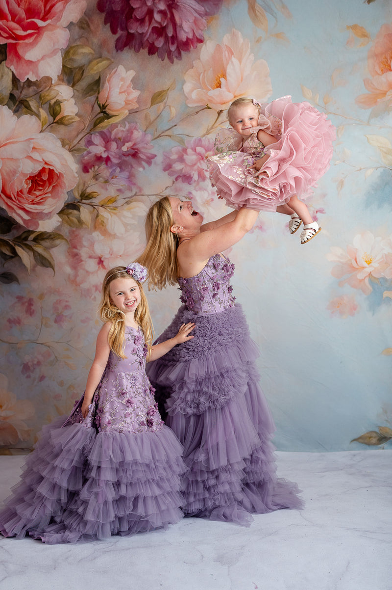 Whimsical mother-daughter moment in matching lavender floral gowns in a dreamy meadow.

