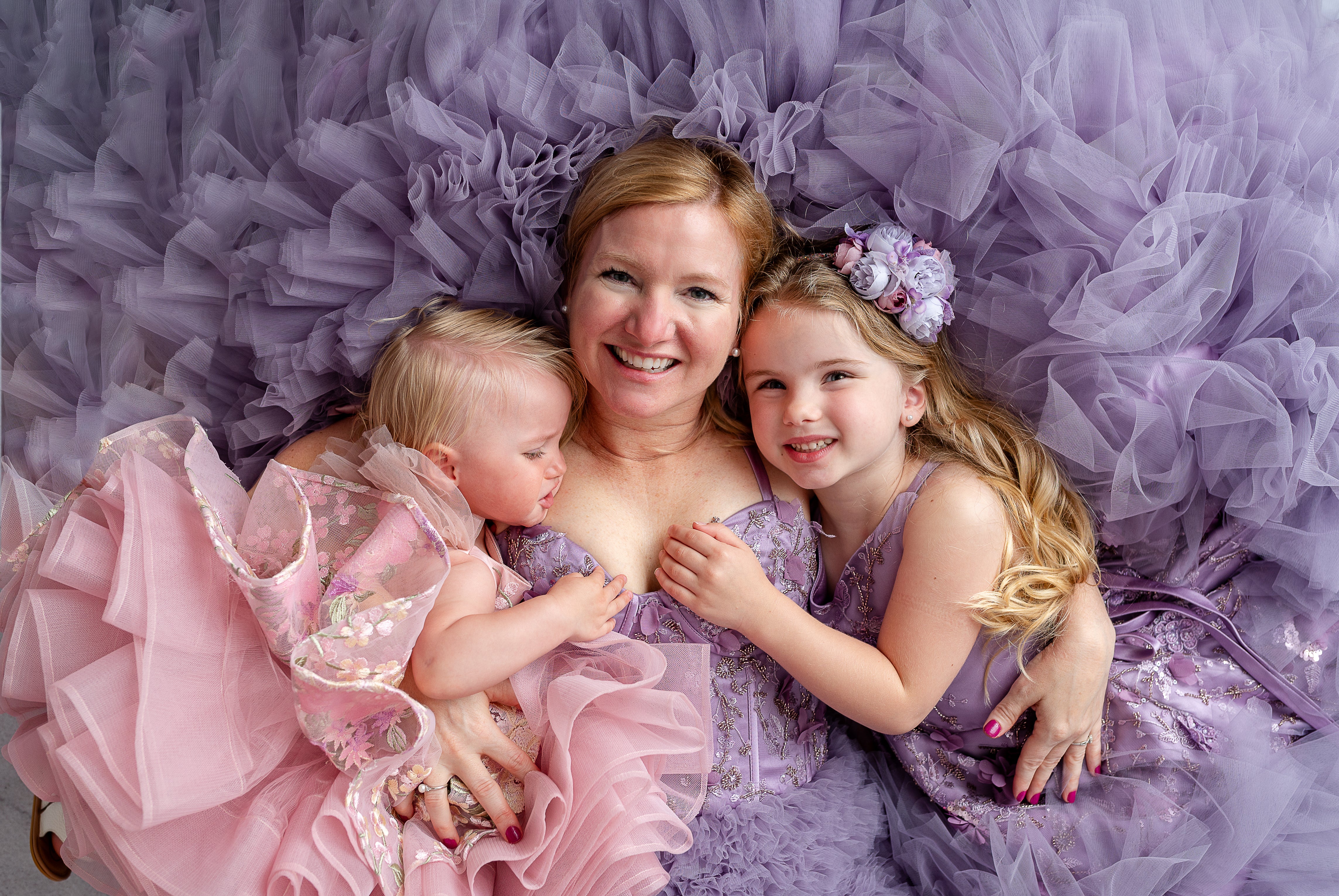 Mother holding hands with daughter wearing floor-length lavender floral tulle dresses.

