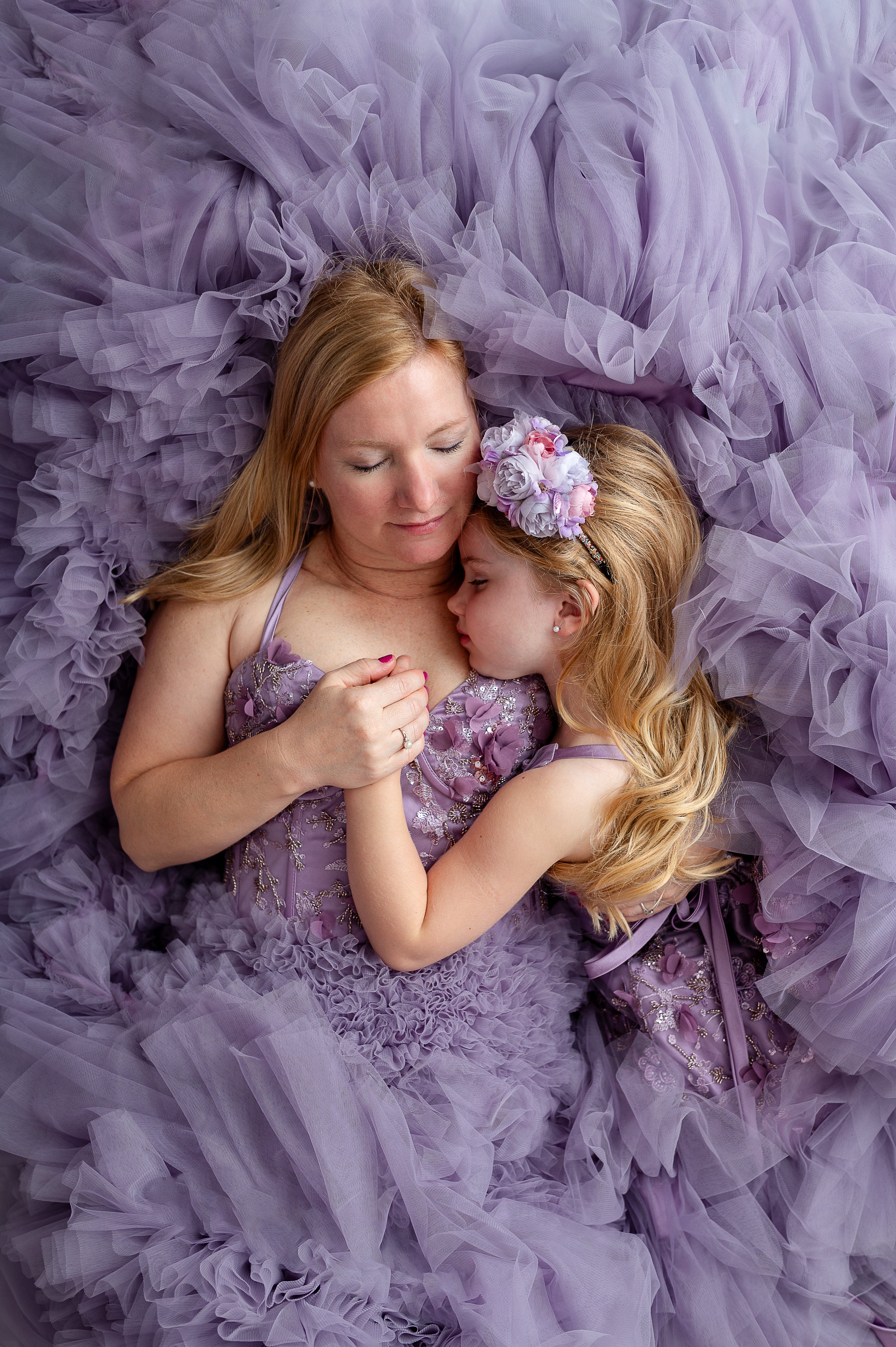 Close-up of mom and daughter embracing in Violet Grace gowns with floral appliqués.

