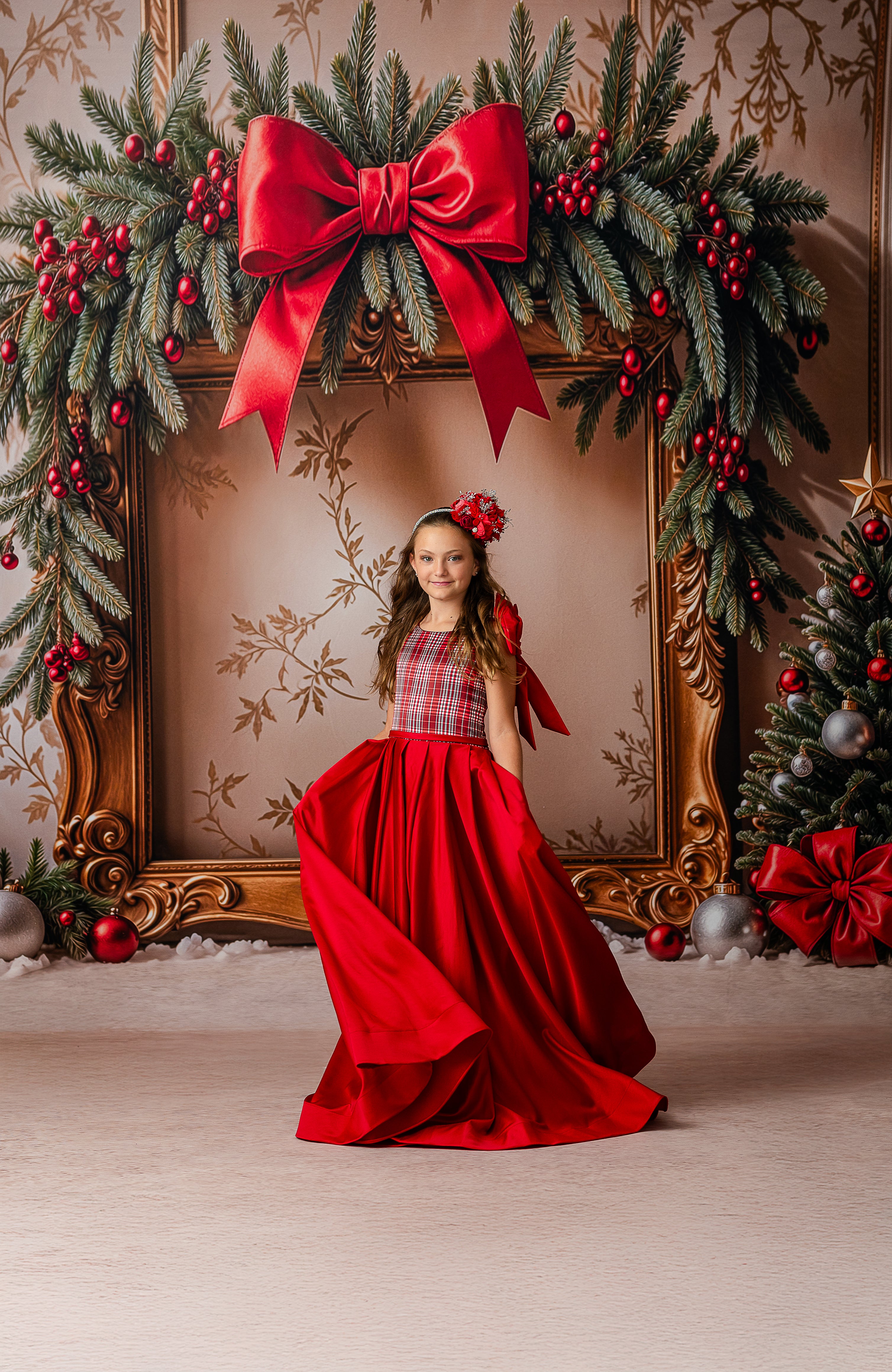 Woman in a red dress standing in front of a decorated Christmas wreath with a large red bow.