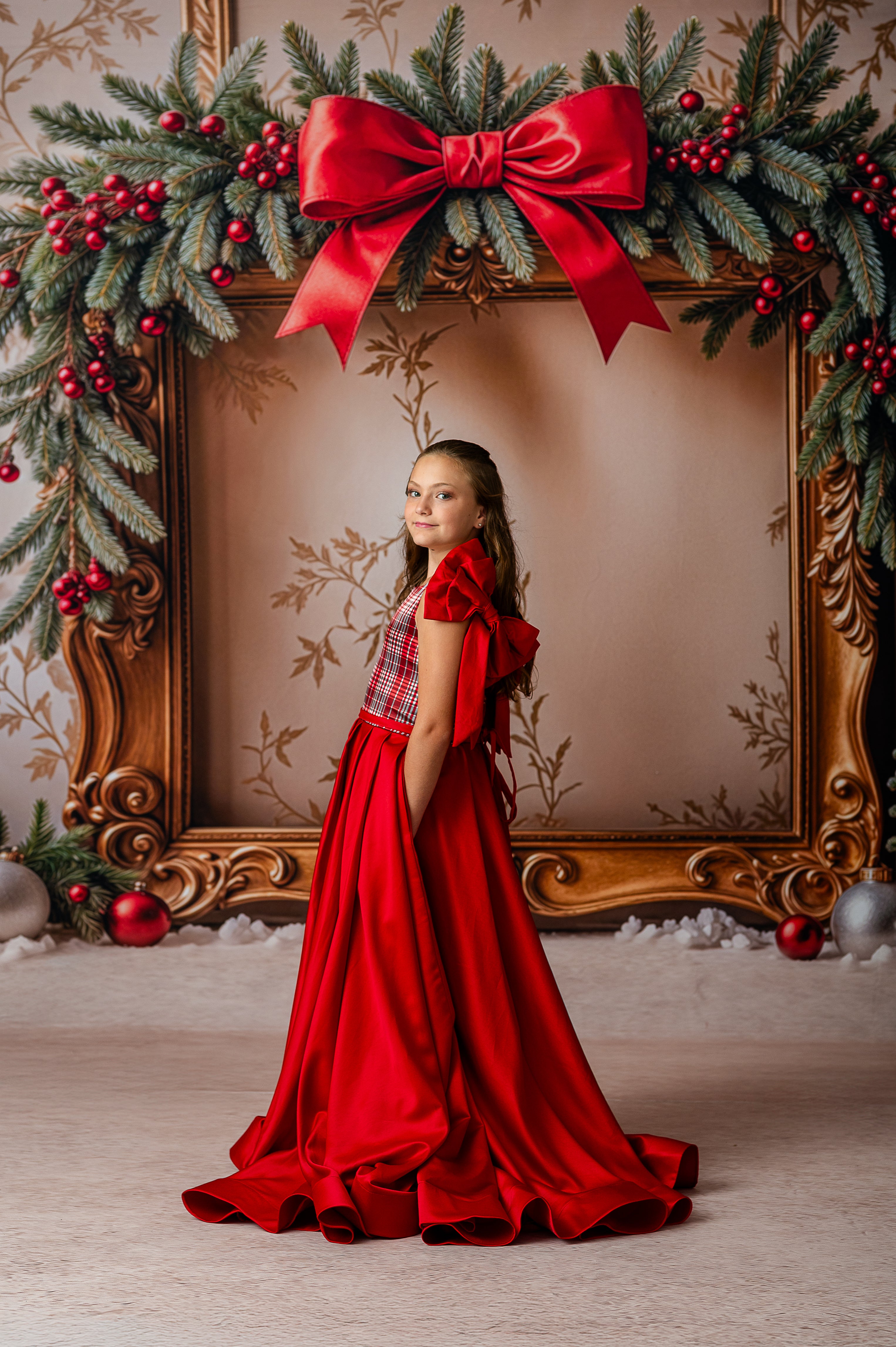 Woman in a red dress standing in front of a decorated frame with a large red bow and Christmas decorations.