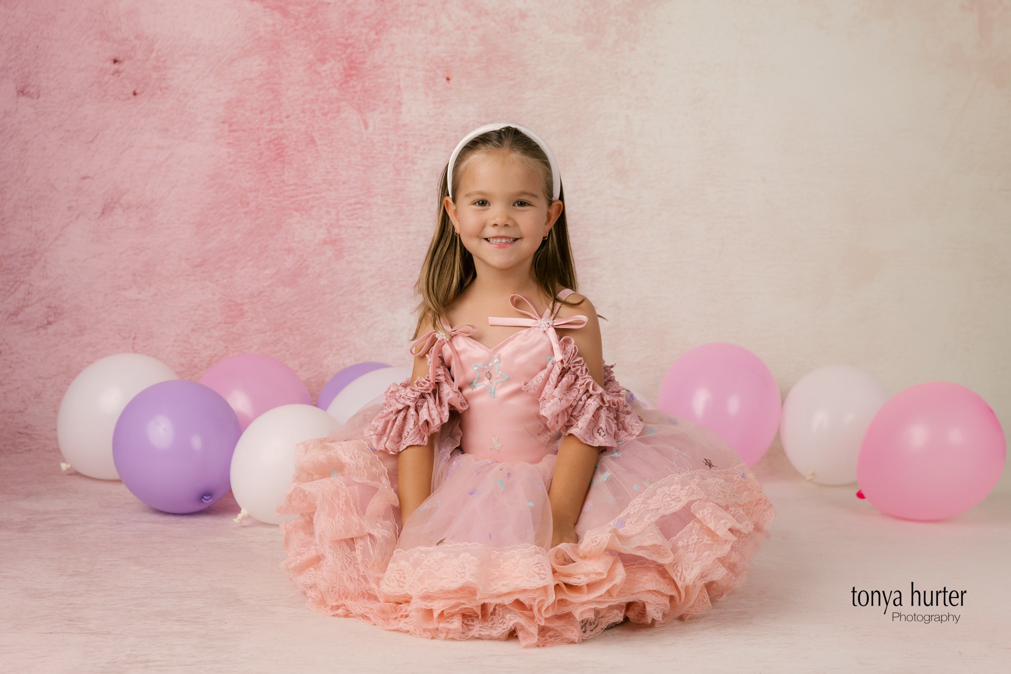 Young girl in a pink dress surrounded by balloons against a pink background