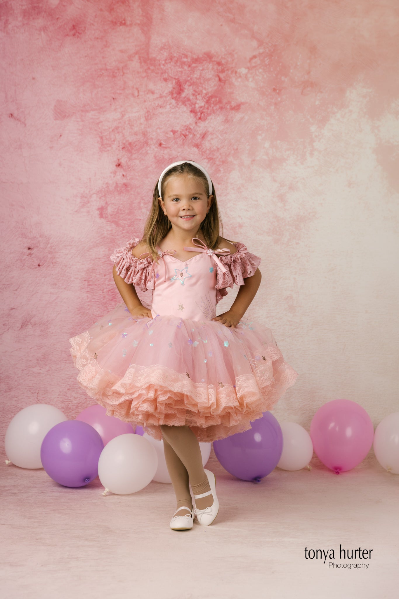 Young girl in a pink dress standing among balloons against a pink background