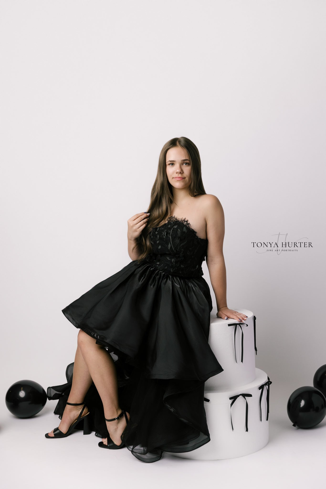 Woman in a black strapless dress posing against a white background with black balloons.