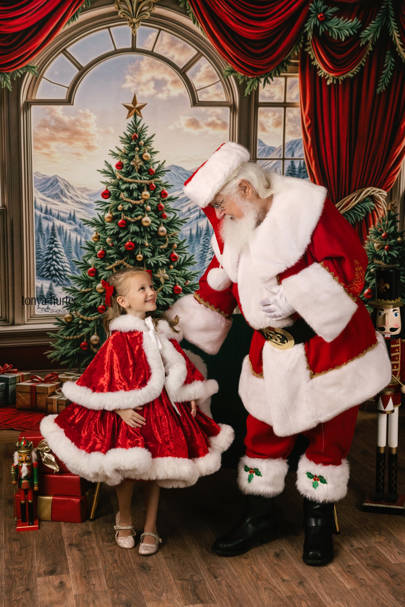 Santa Claus and a child in matching red outfits in a festive room with Christmas decorations.