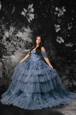 Woman in a blue gown against a dark floral backdrop