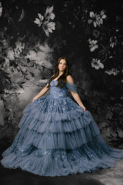 Woman in a blue gown against a dark floral backdrop