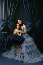 Two women in elegant dresses posing against a dark curtain backdrop