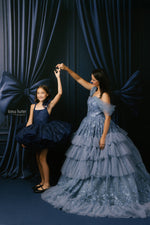 Woman and young girl in formal dresses posing against a dark curtain backdrop