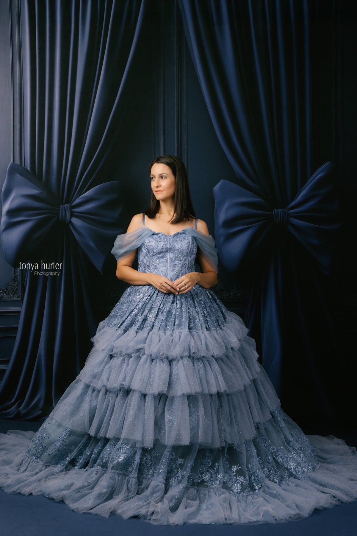 Woman in a blue lace dress standing against a dark blue curtain backdrop