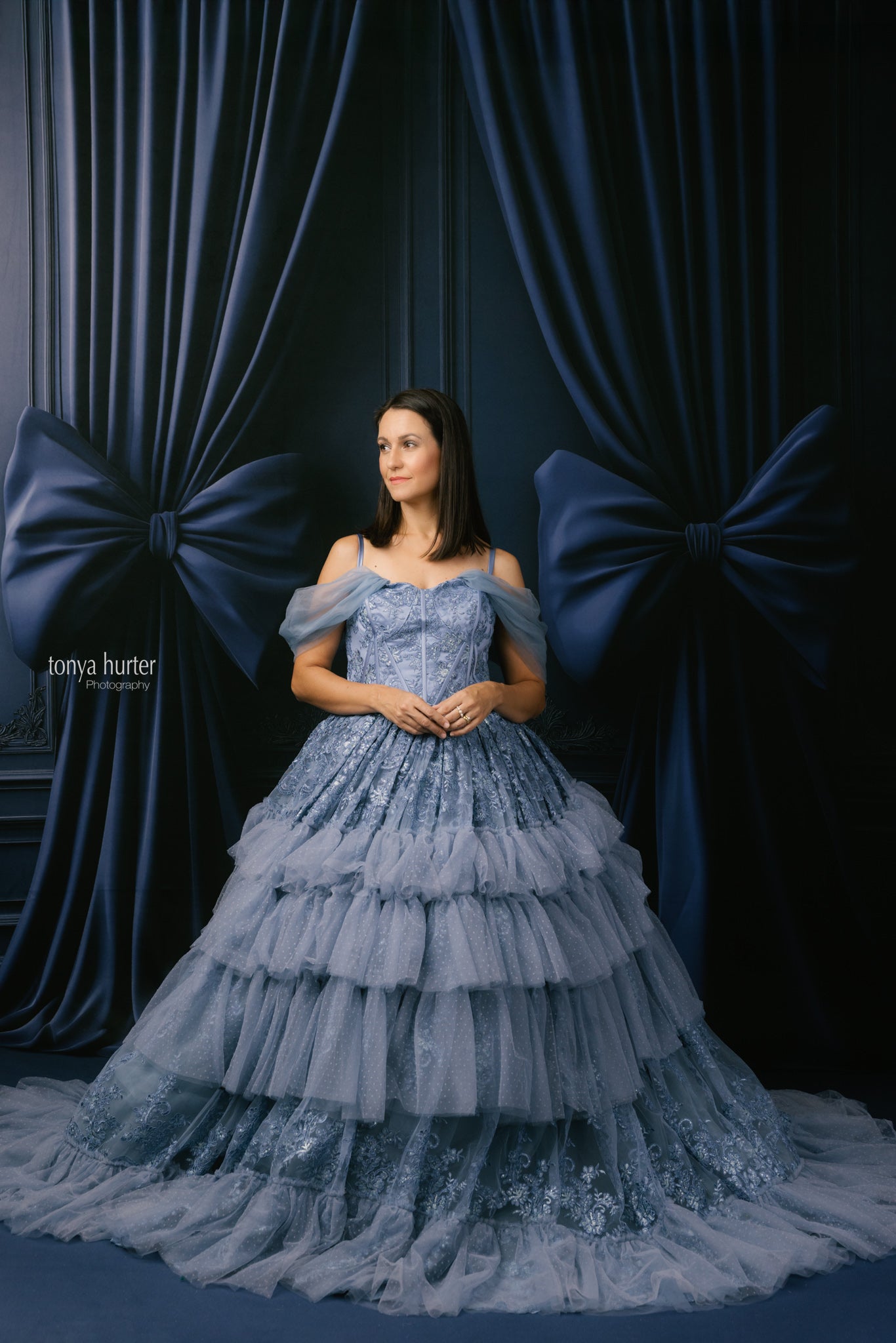 Woman in a blue lace dress standing against a dark blue curtain backdrop