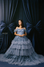 Woman in a blue lace dress standing against a dark blue curtain backdrop