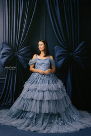 Woman in a blue lace dress standing against a dark blue curtain backdrop
