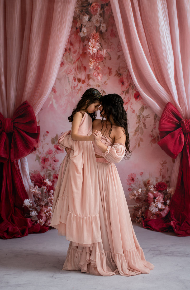 Two women in elegant dresses standing in front of a floral and curtain backdrop