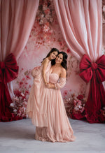Two women in elegant dresses standing in front of a decorative floral and curtain backdrop.