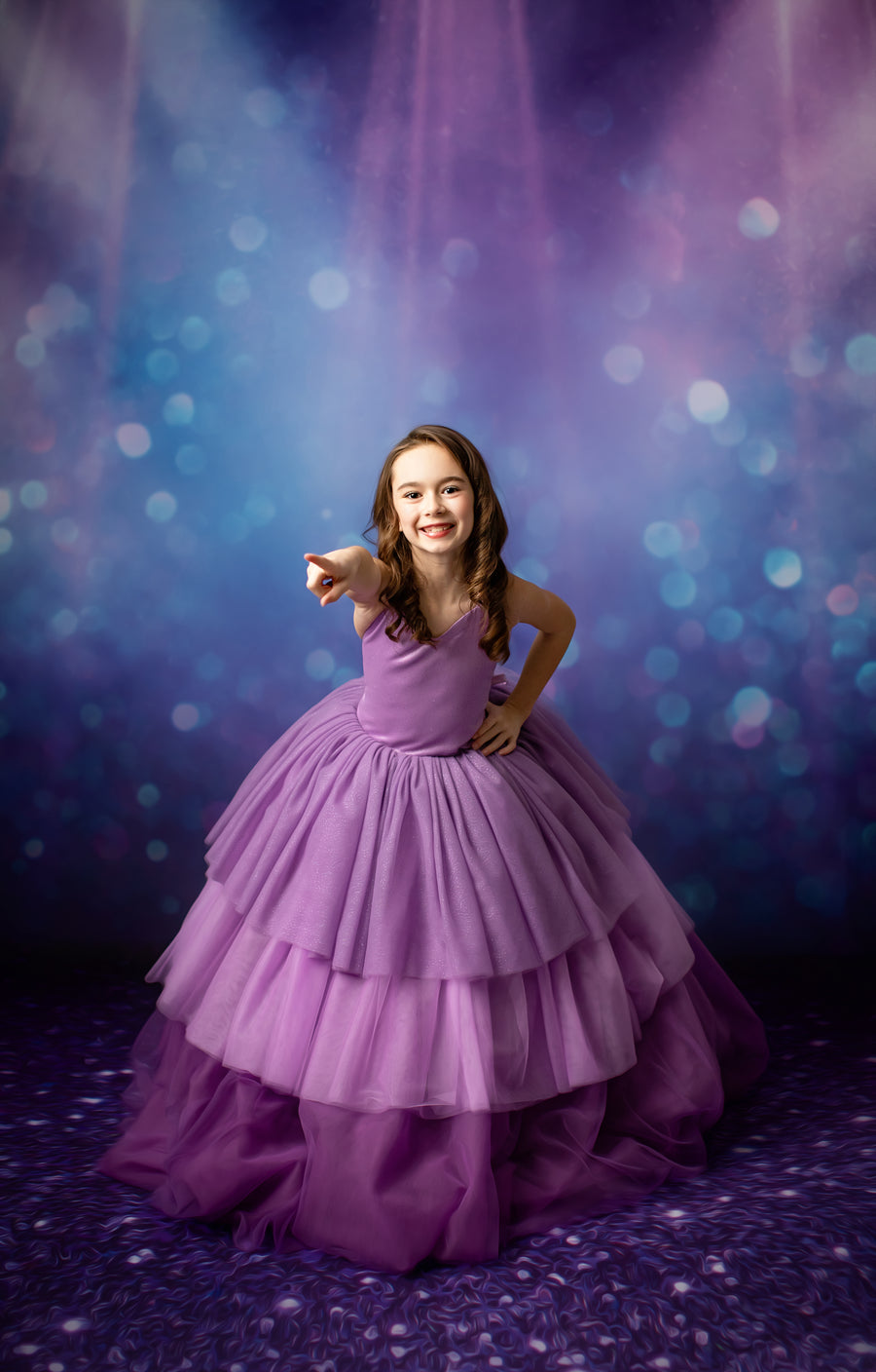 Little girl in a flowing lavender gown sings into a microphone, bathed in dramatic stage lighting.