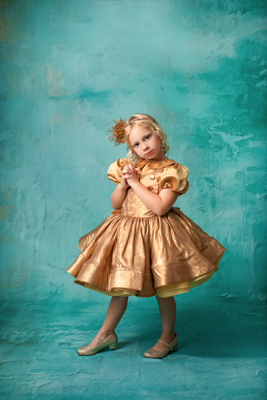 "Girl in a luxurious gold gown with dramatic puff sleeves, posing gracefully."
