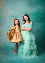 "Girl in a flowing mint green gown standing against a teal backdrop."
